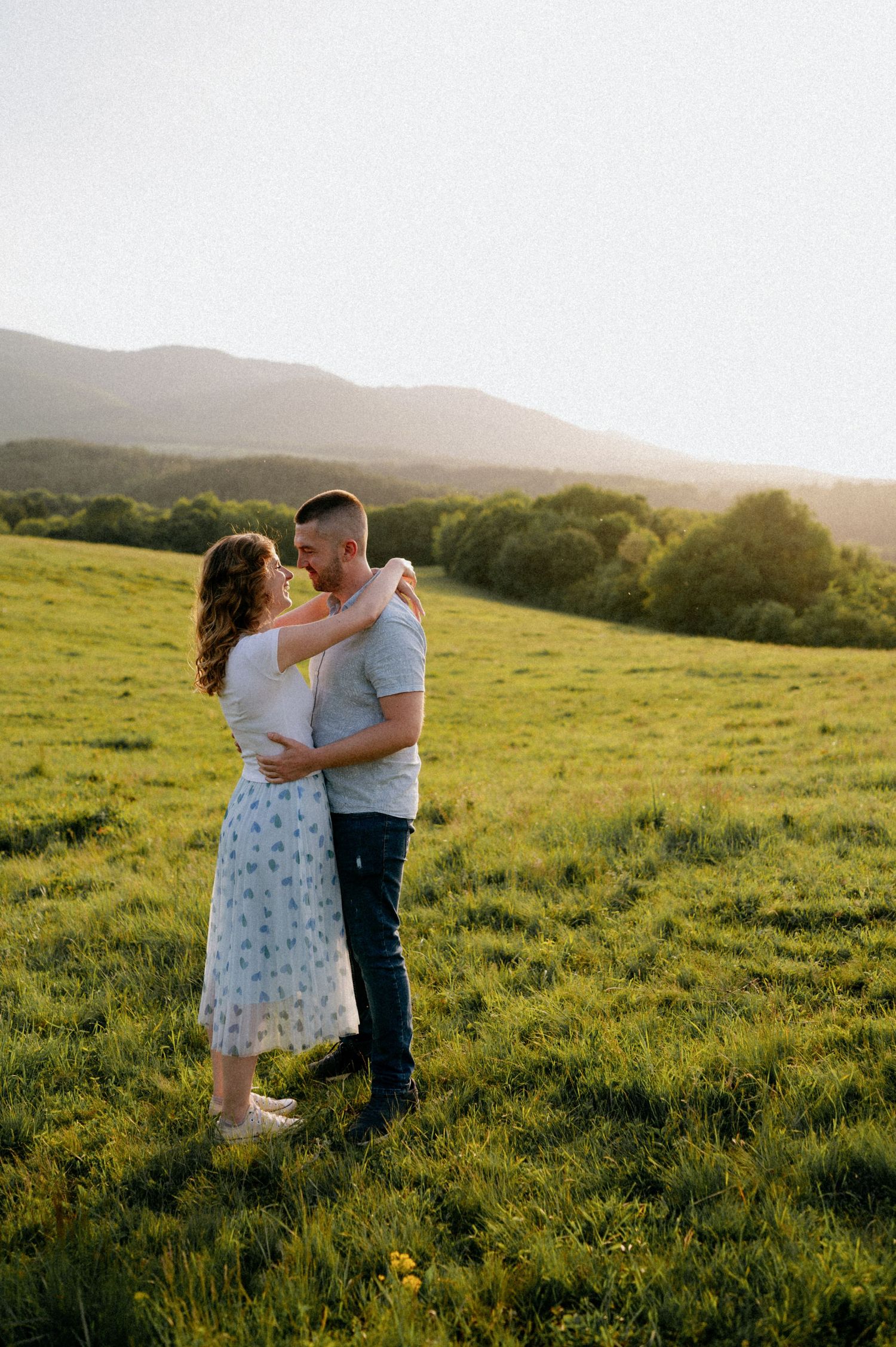 A romantic couple embraces in a grassy field during golden hour.