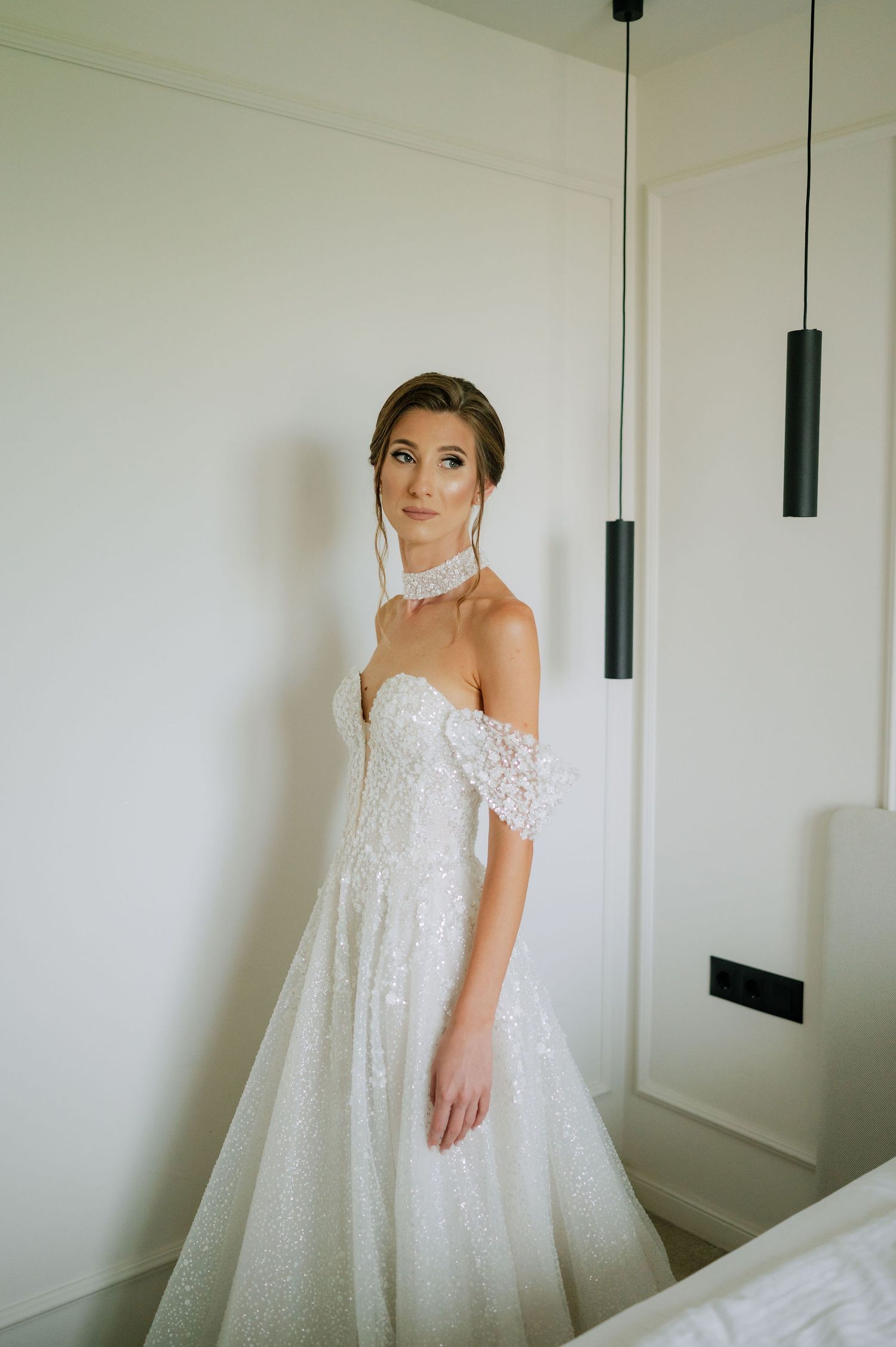 Full-length view of a flowing white wedding gown with lace detailing in a minimalist room.