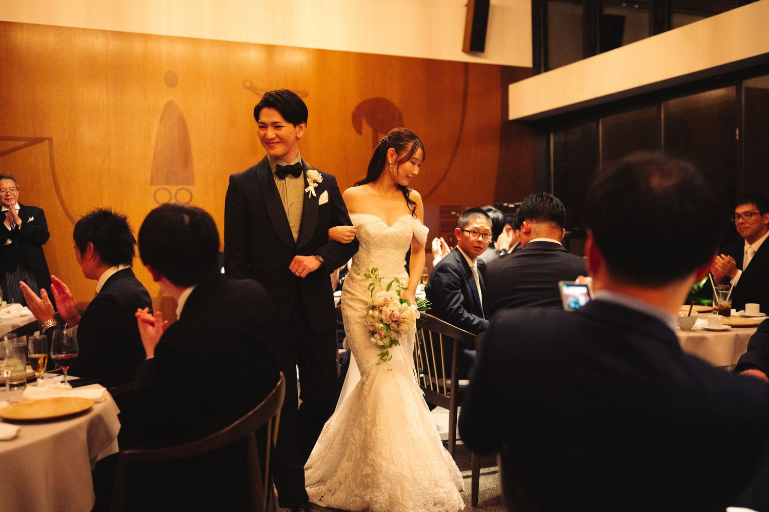 Wedding couple and guests celebrate in a warmly lit reception venue with elegant decor and lighting.