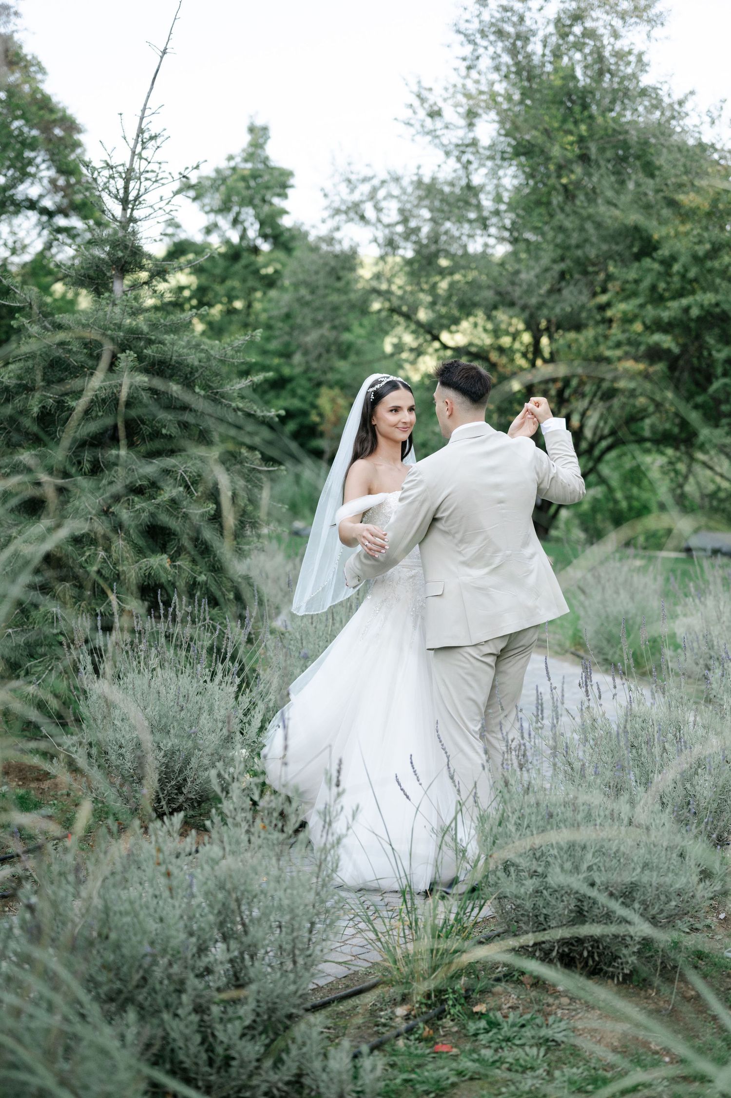 A couple dances together in a field of lavender, with the bride wearing a white gown and groom in light suit.