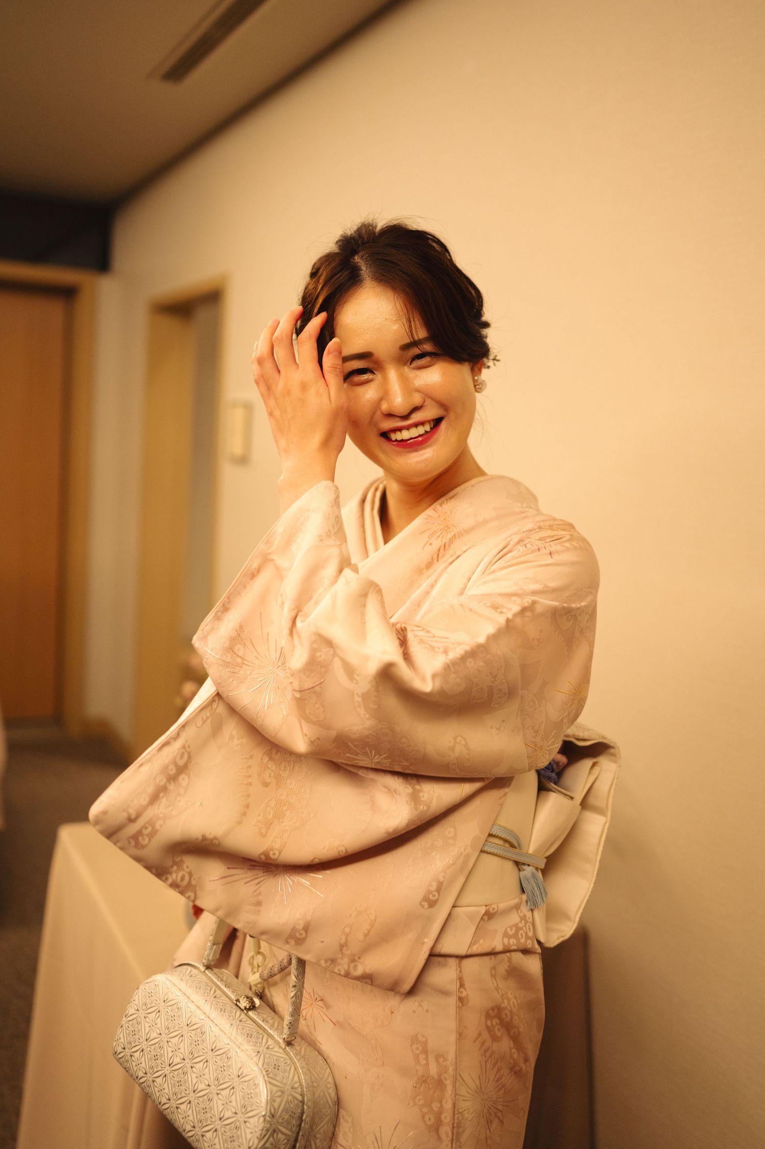 Person in pink kimono poses playfully with silver bag against neutral background.