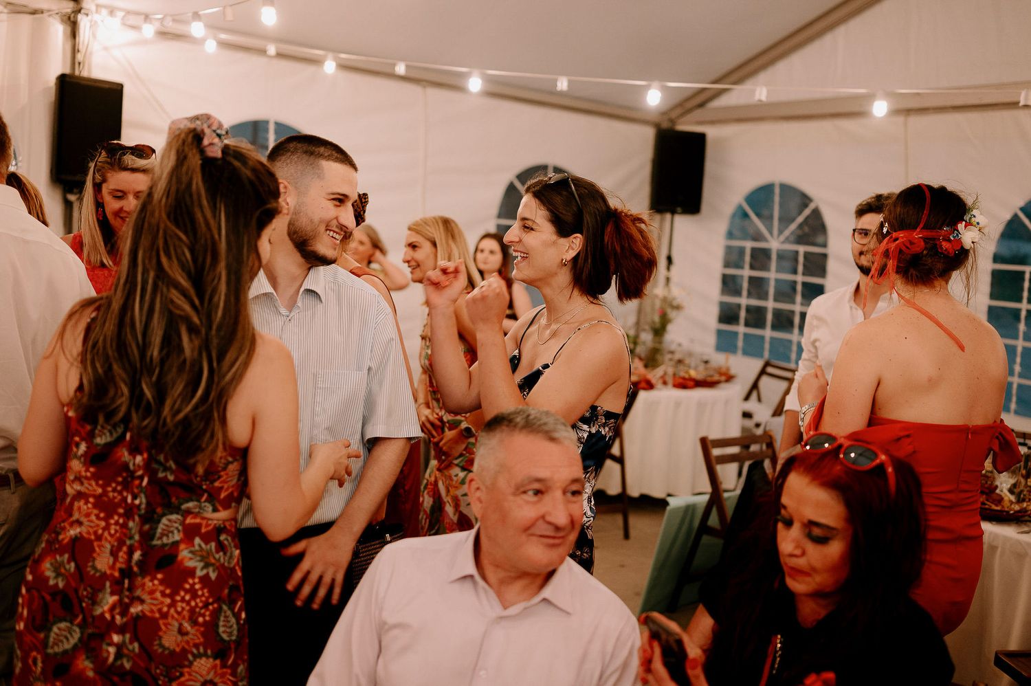 Wedding guests dance and celebrate together under string lights in a white tent reception venue.