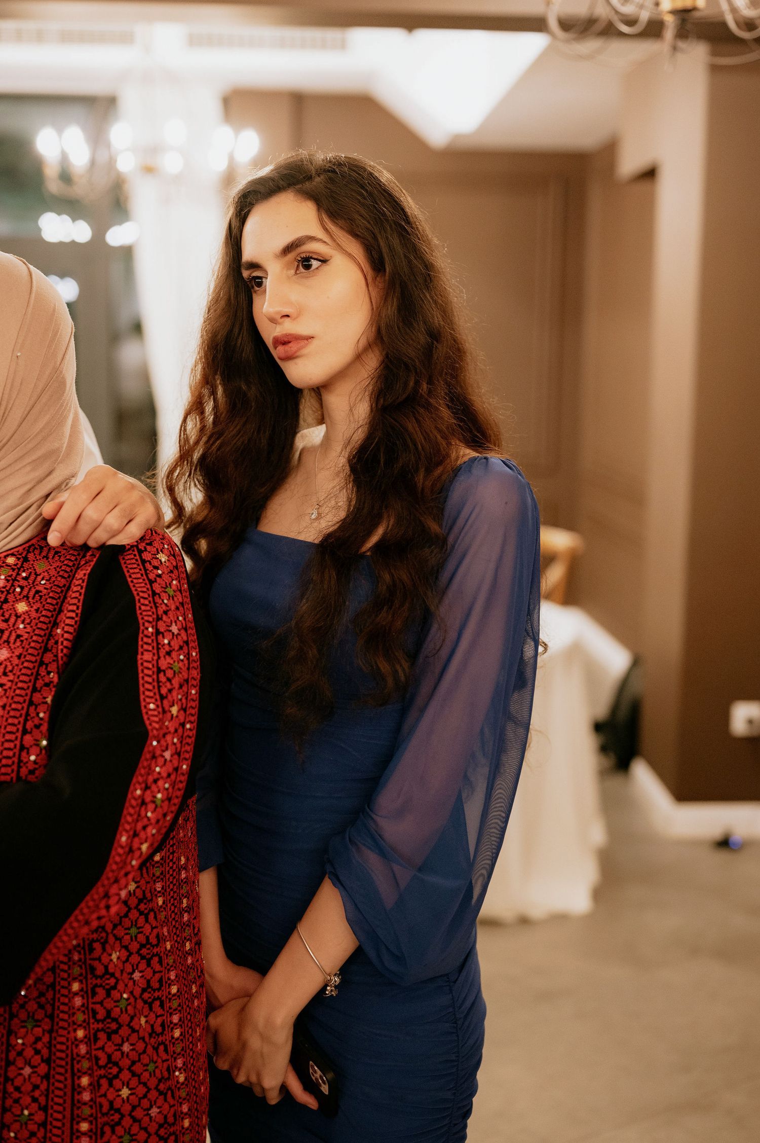 Woman in navy dress and red sequined jacket poses elegantly in an indoor setting.