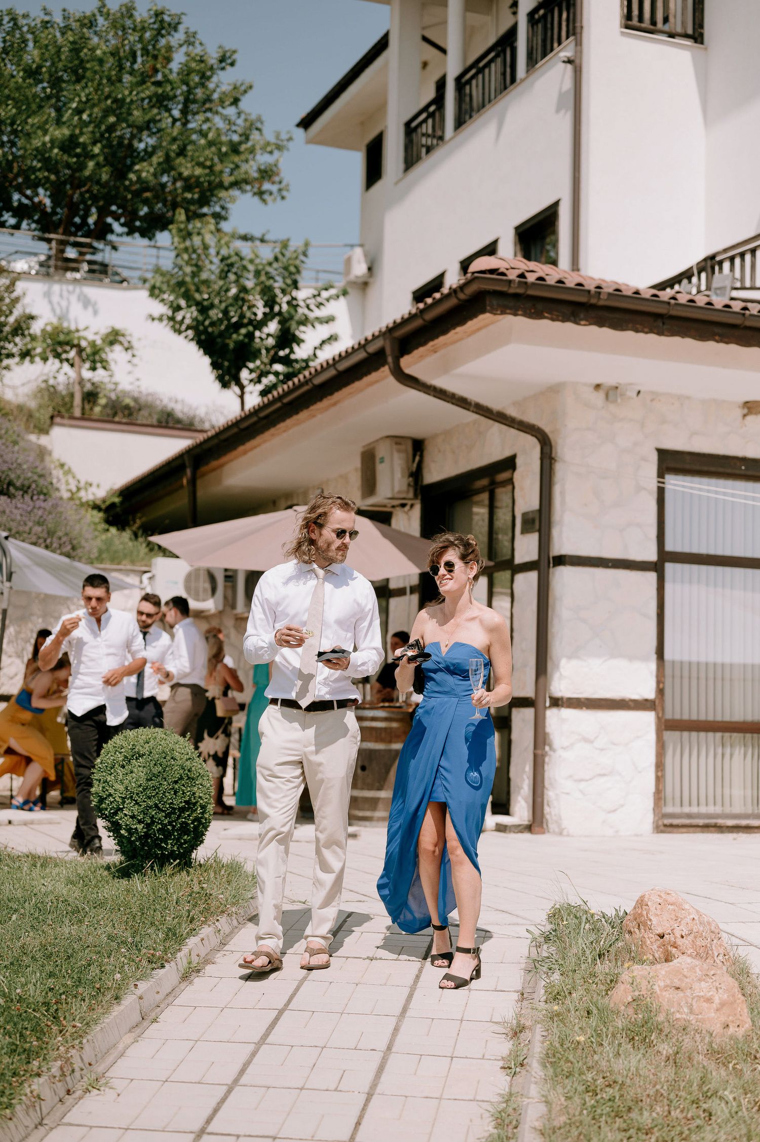 Guests in formal attire walking along a white building exterior during an event.