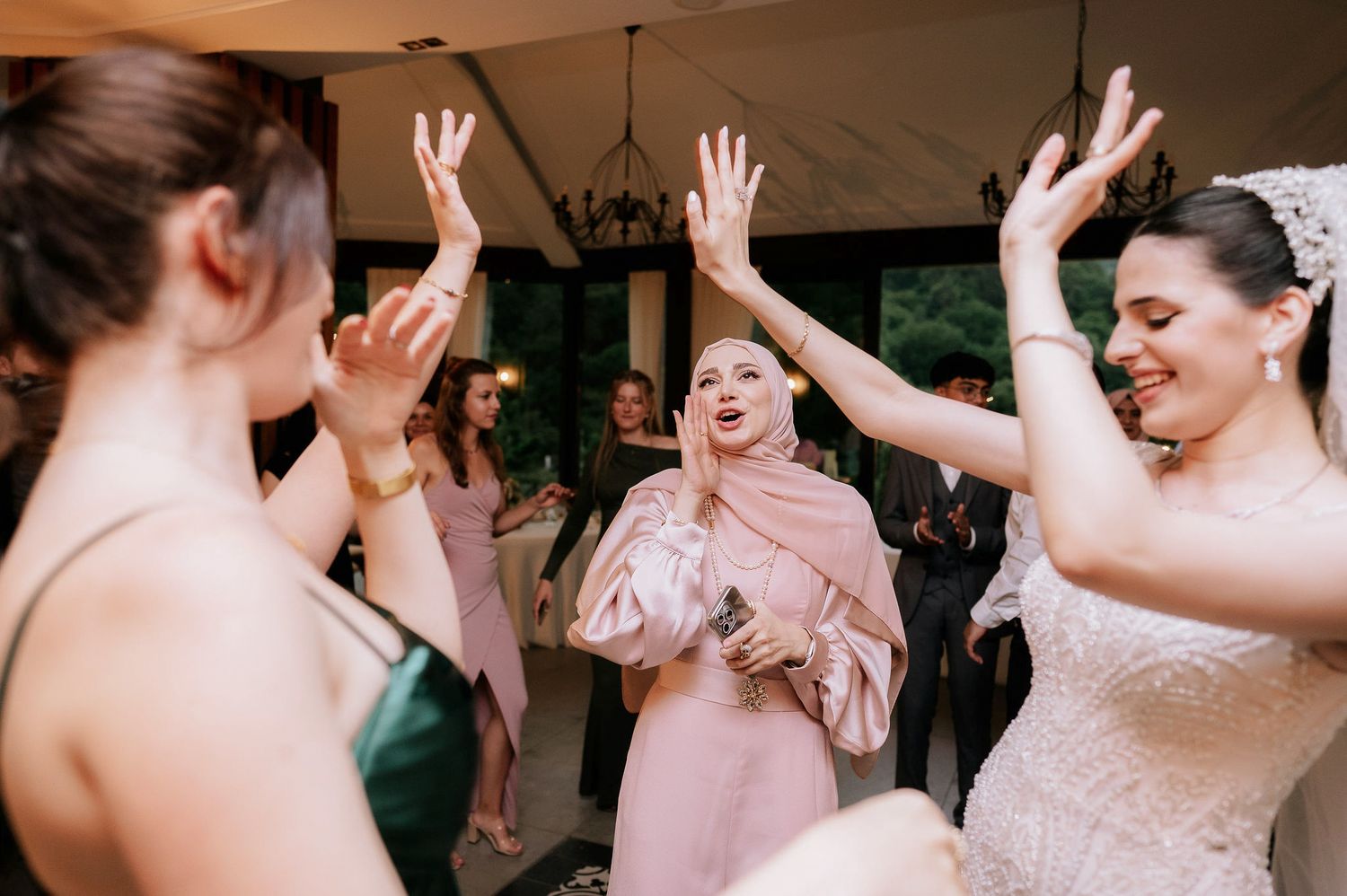 Energetic wedding reception scene with people dancing and raising their hands in celebration.