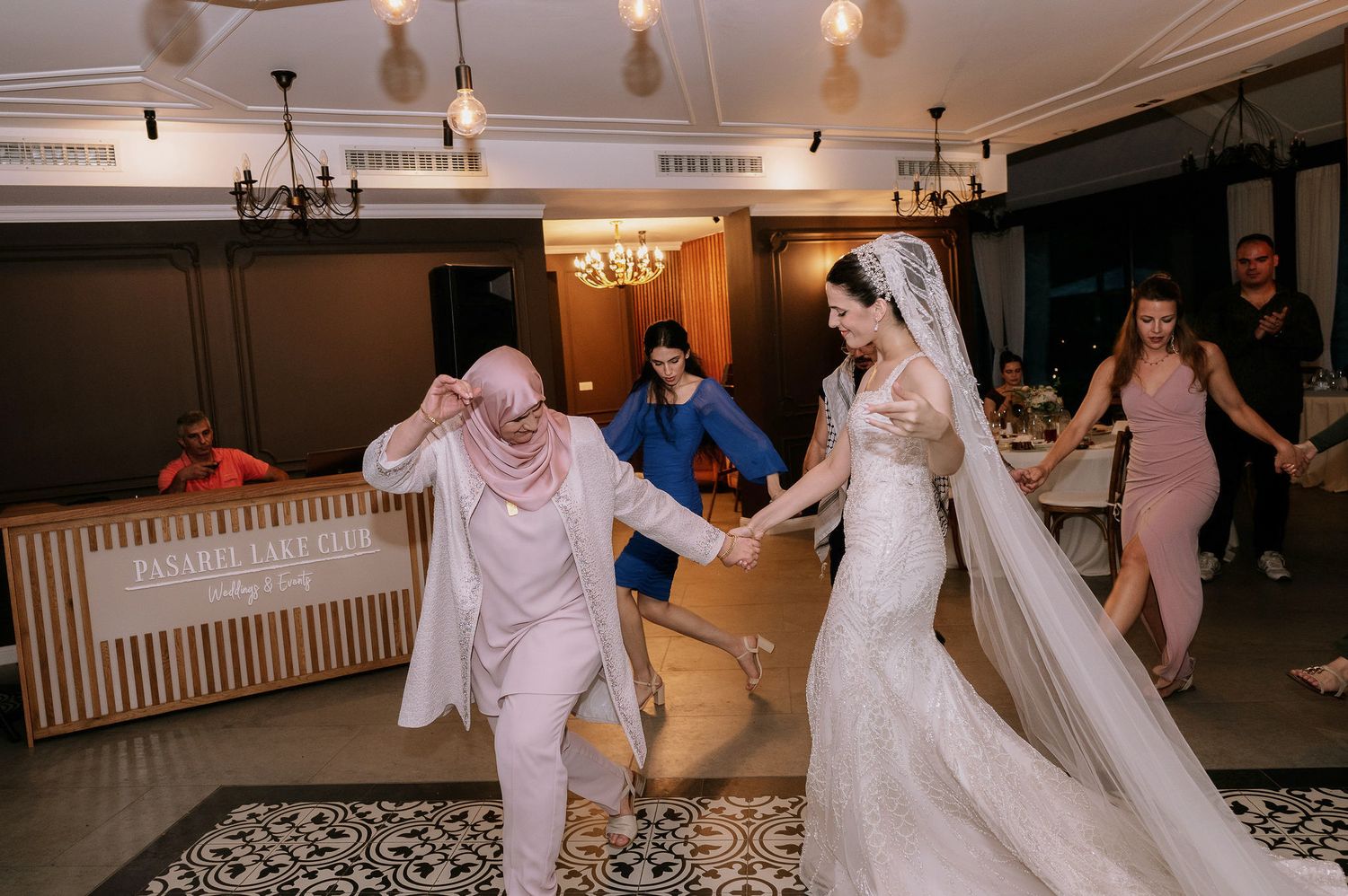 Wedding reception guests dancing together in a bright indoor venue with pendant lighting.
