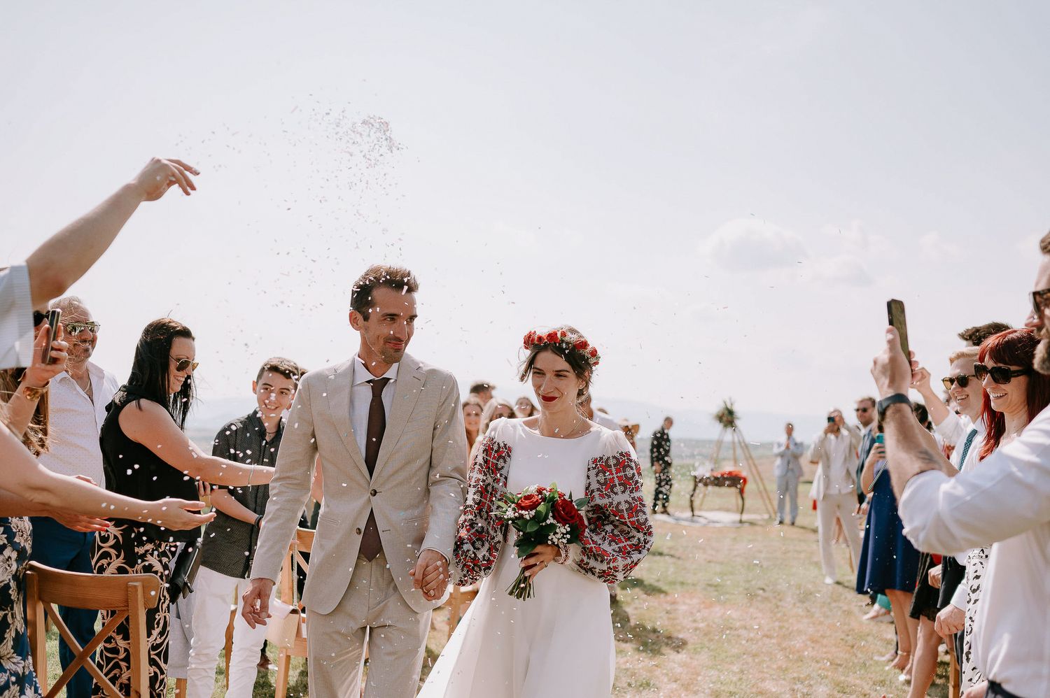 Wedding celebration captured in panoramic view with guests gathered on a sunny hillside.