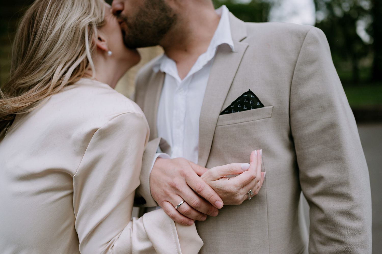 A couple in cream colored outfits share a tender moment outdoors.