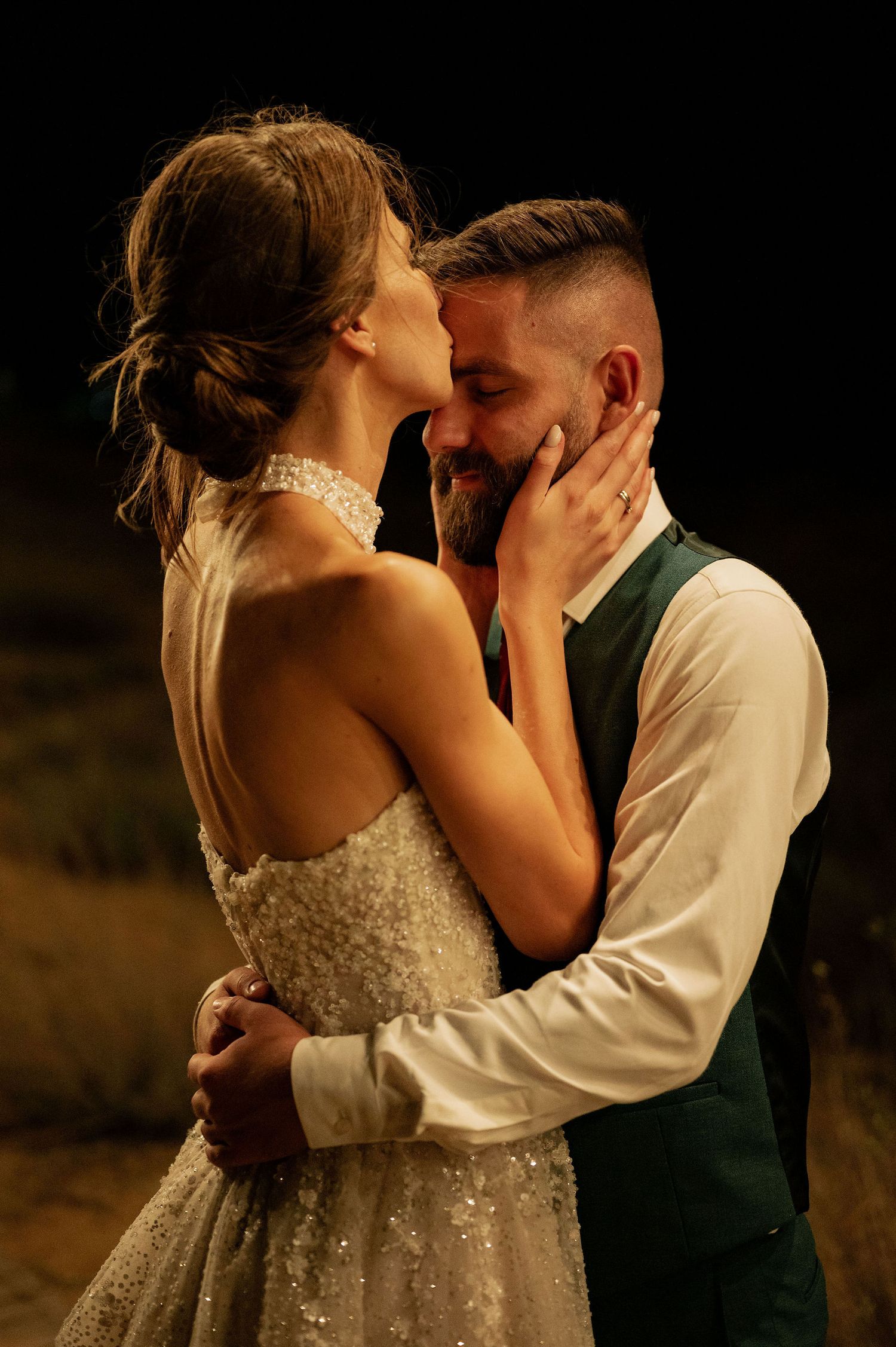 A romantic embrace captured under warm string lights during a nighttime wedding celebration.