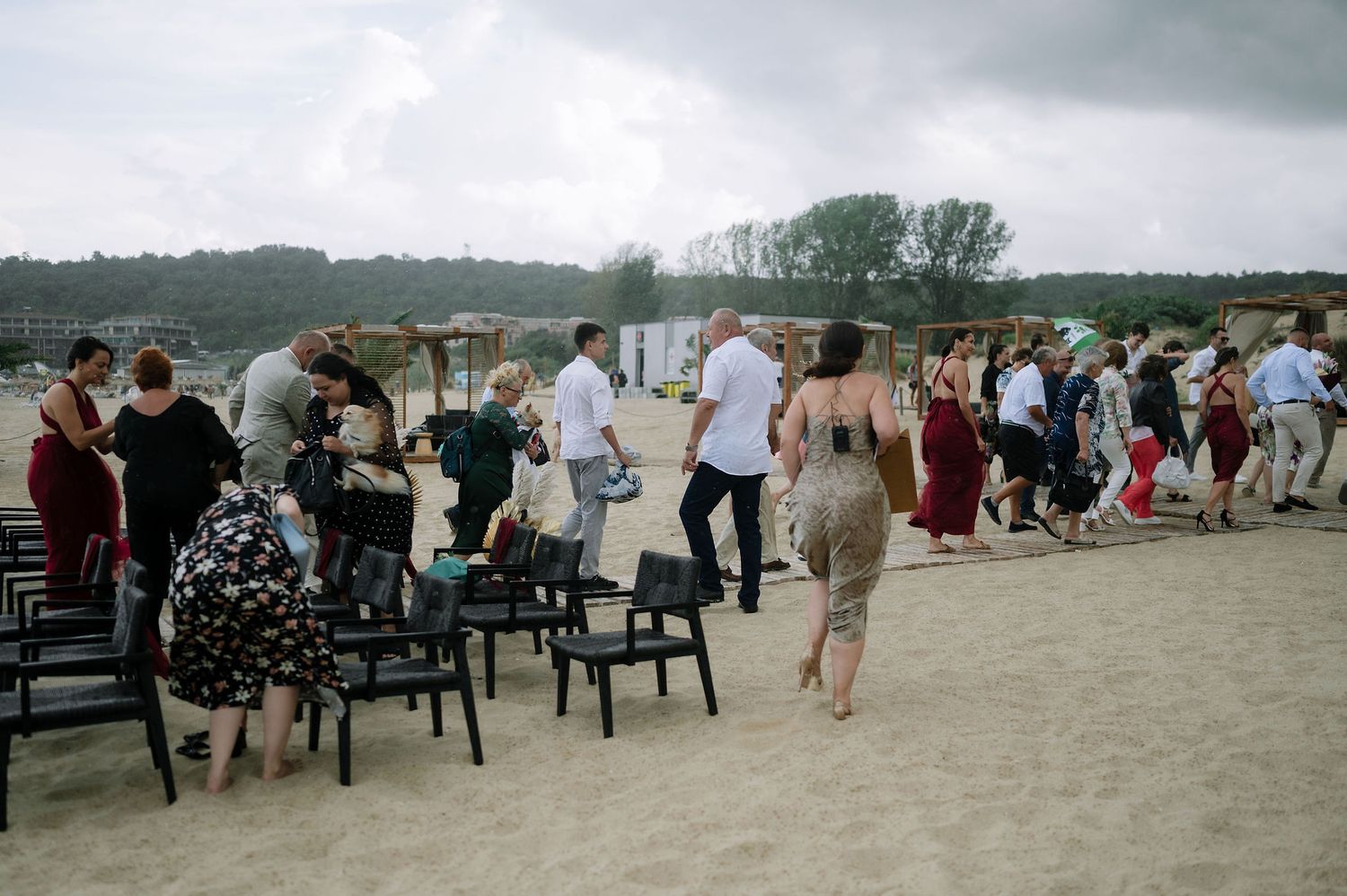 Wide shot of wedding guests seated on chairs along a beach with cloudy skies overhead.