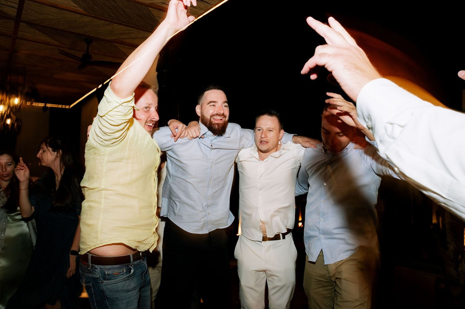 Group of friends celebrating with raised arms and excited expressions at a nighttime party.