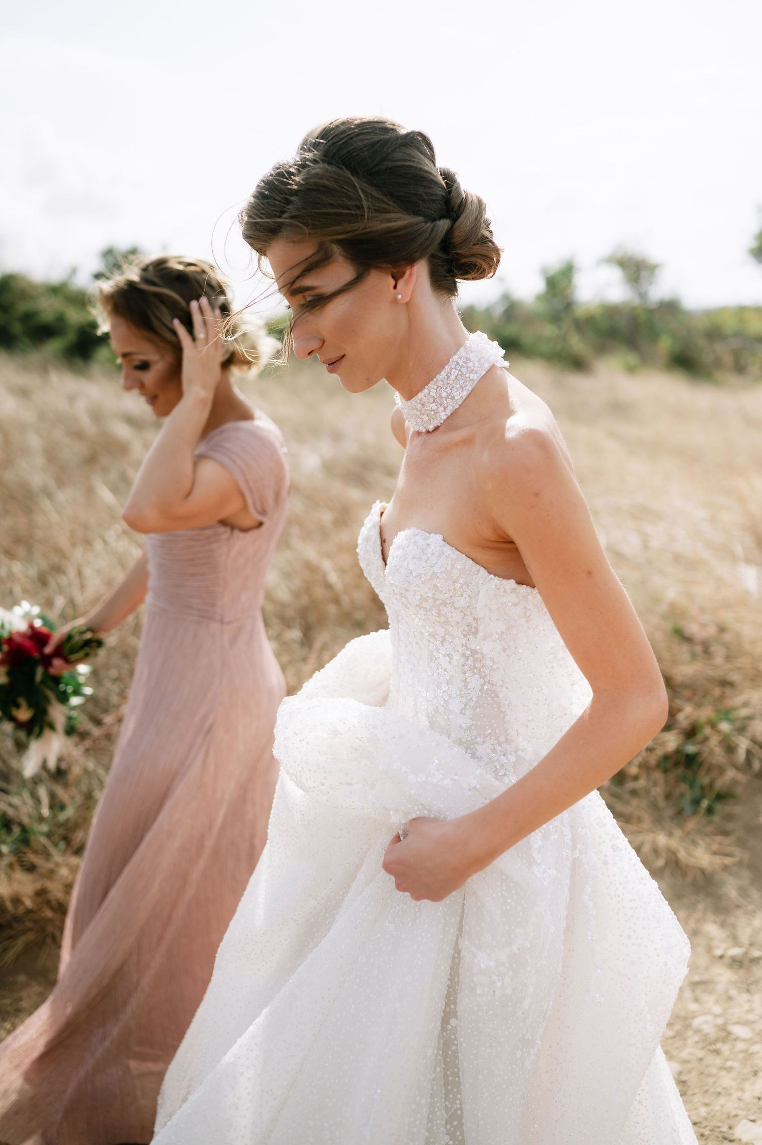 Two figures in contrasting dresses share a joyful moment on a sunny outdoor path.