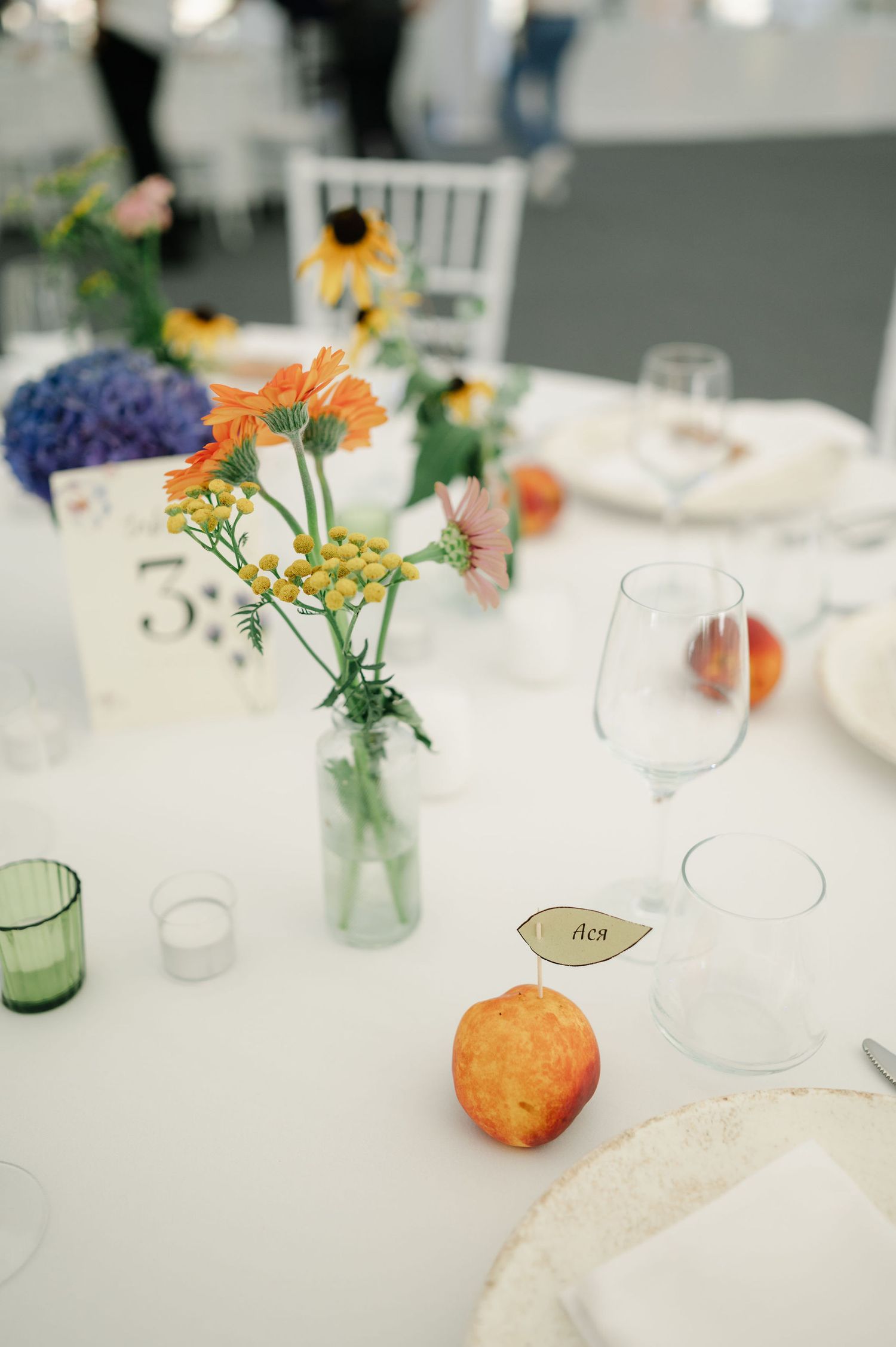 Wedding reception table decorated with small vases of colorful wildflowers and white place settings.