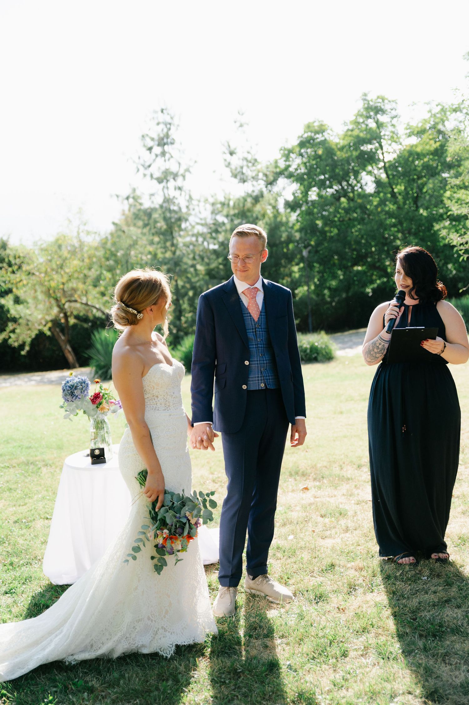 Wedding participants gather in a grassy field during a sunny outdoor ceremony.
