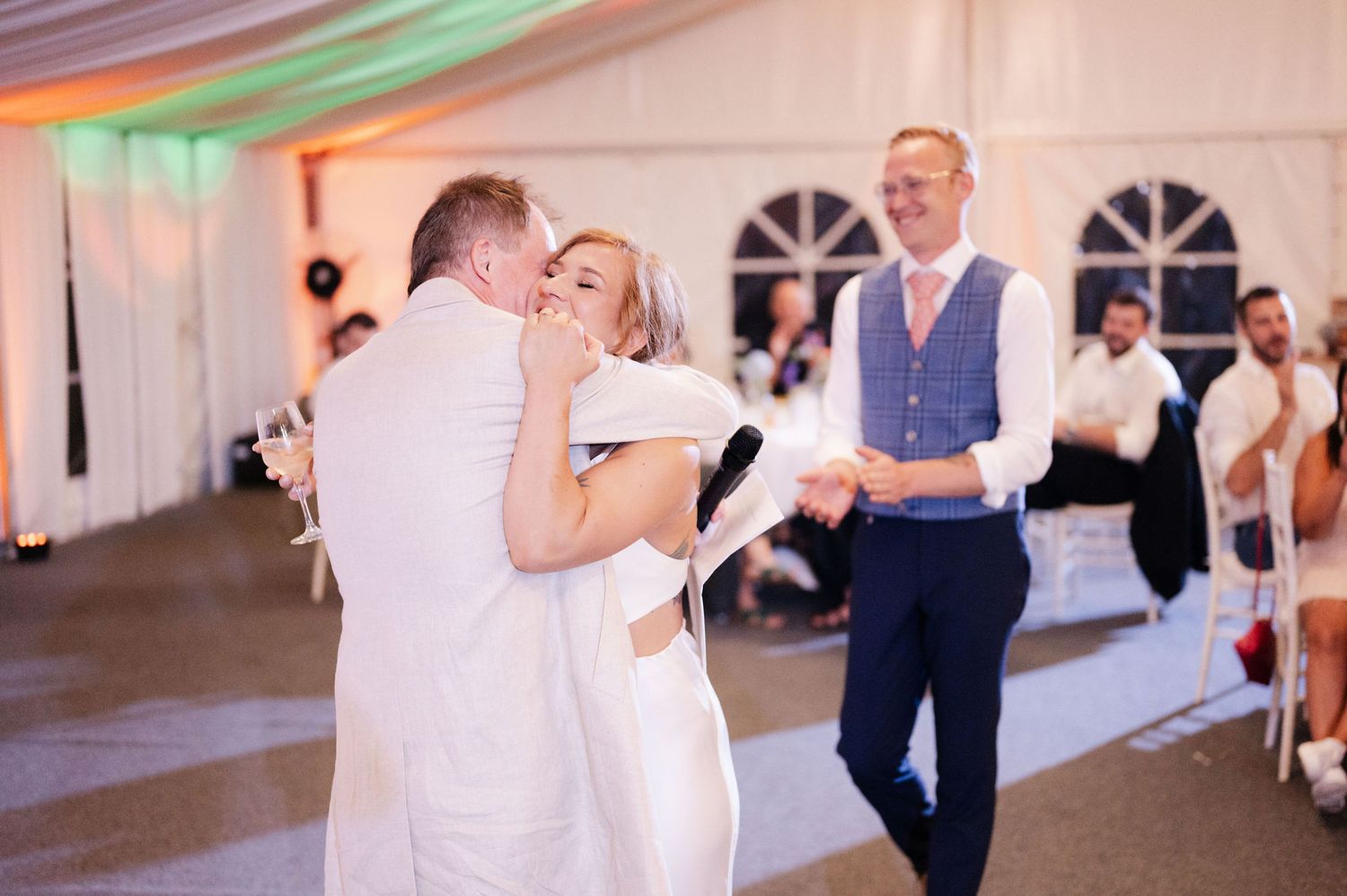 Wedding celebration with guests dancing under string lights in an elegant white tent venue.