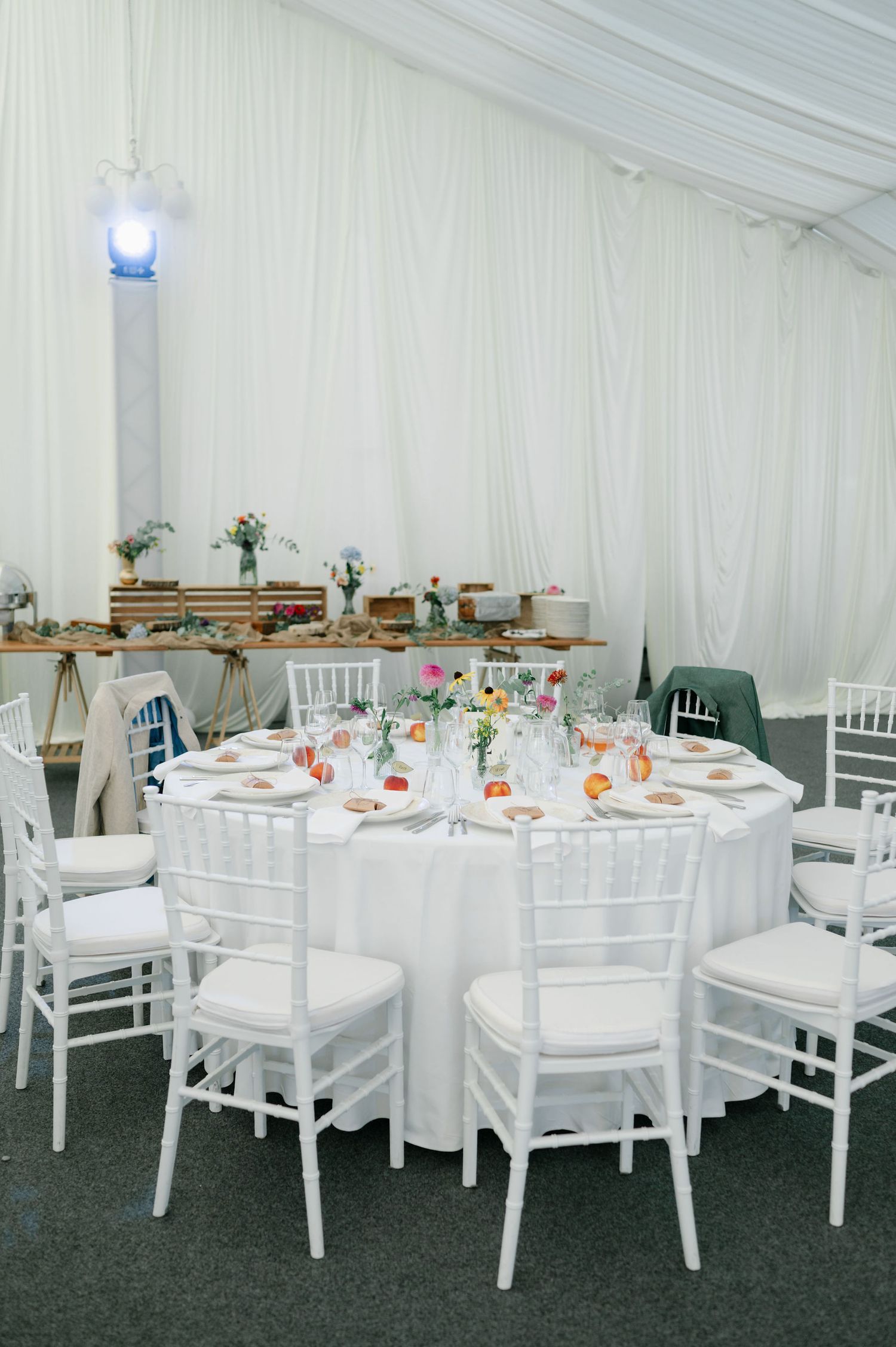 Interior of wedding tent showing round tables with white linens and chairs arranged for reception.