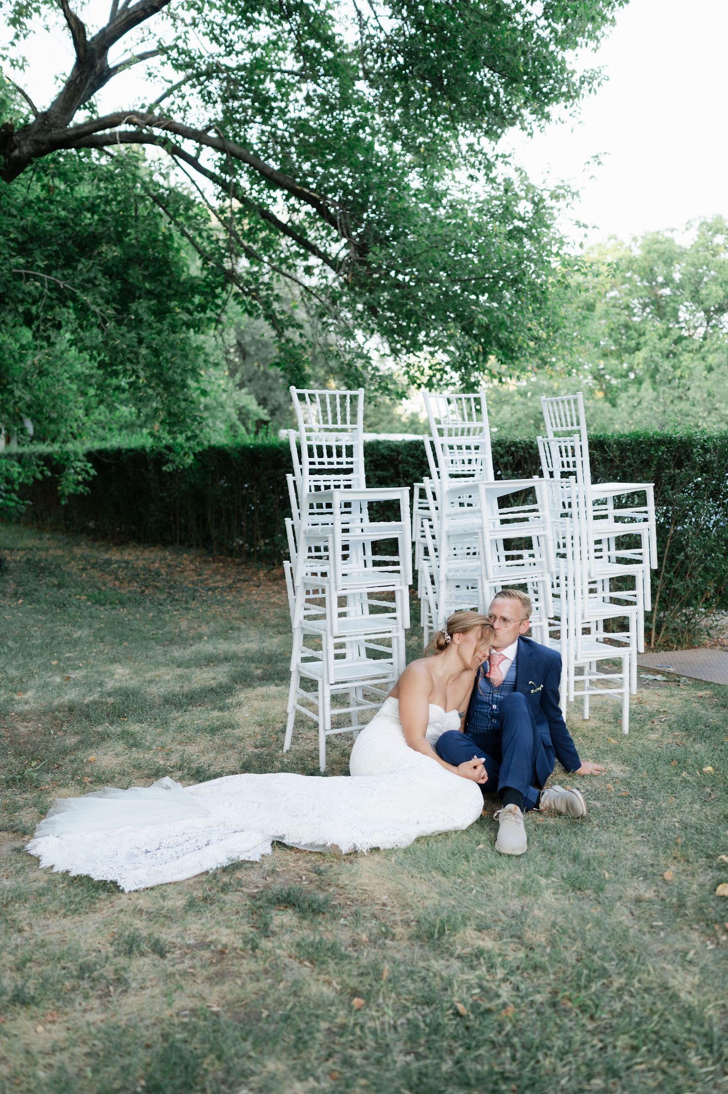 A couple shares an intimate moment on the lawn with white wedding chairs arranged in the background.