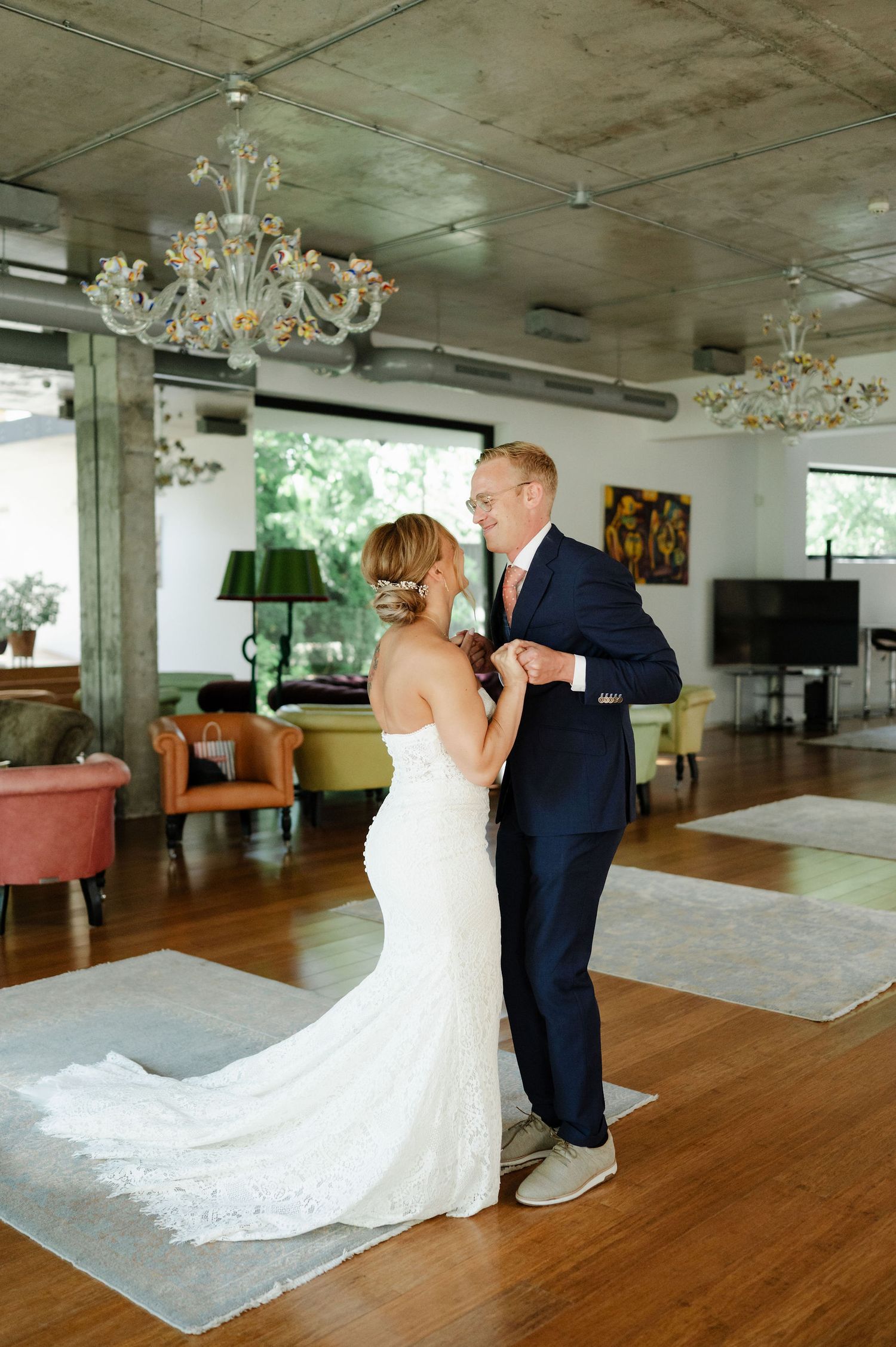 A bride and groom dance together in a spacious room with elegant decor and natural lighting.