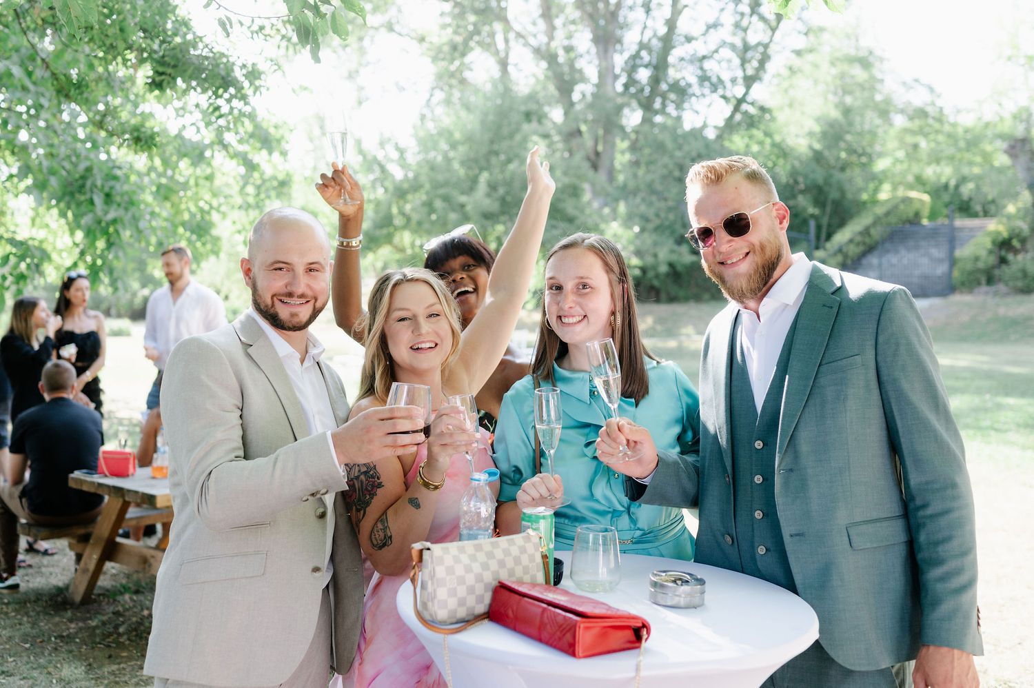 Wedding guests mingling and celebrating at an outdoor reception under trees.