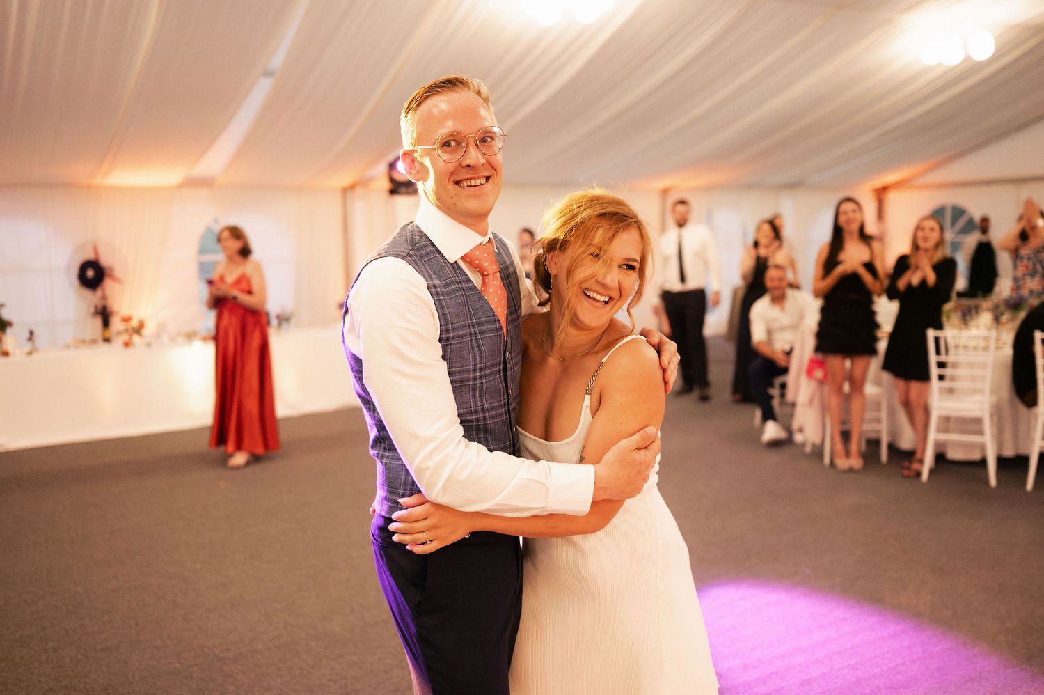 Couples dance together during a wedding reception under elegant white tent draping.