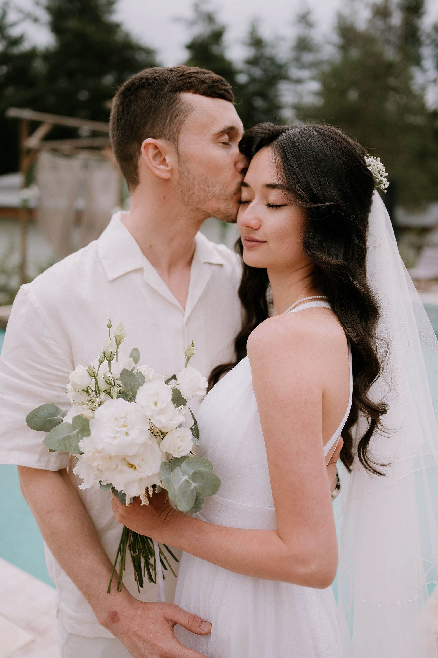 Tender wedding portraits by a swimming pool with white floral and eucalyptus bouquet.