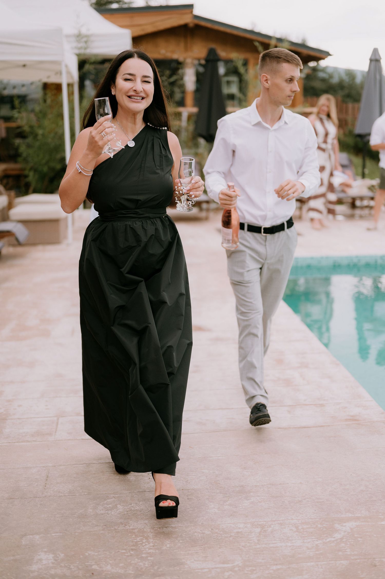 People in formal wear mingling around a pool deck during an outdoor event.