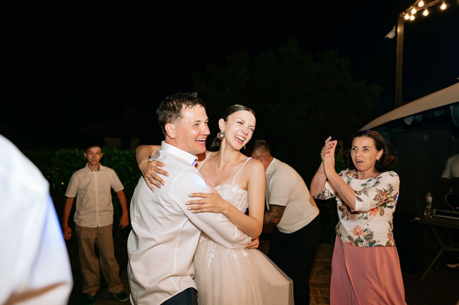 Wedding guests dance together under string lights at an outdoor reception.