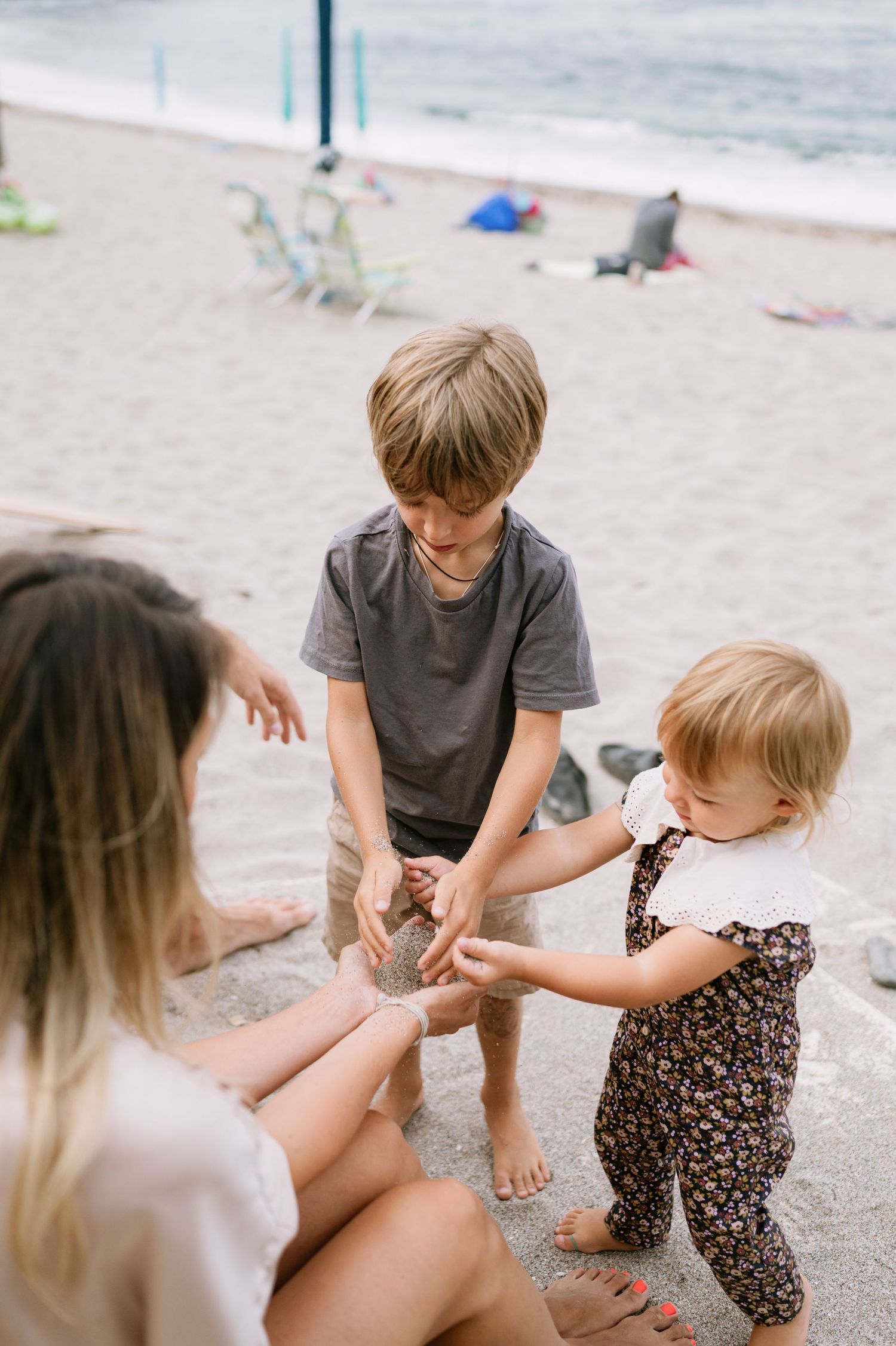 A woman and boy play with a toddler girl in the sand at a beach on a cloudy day.