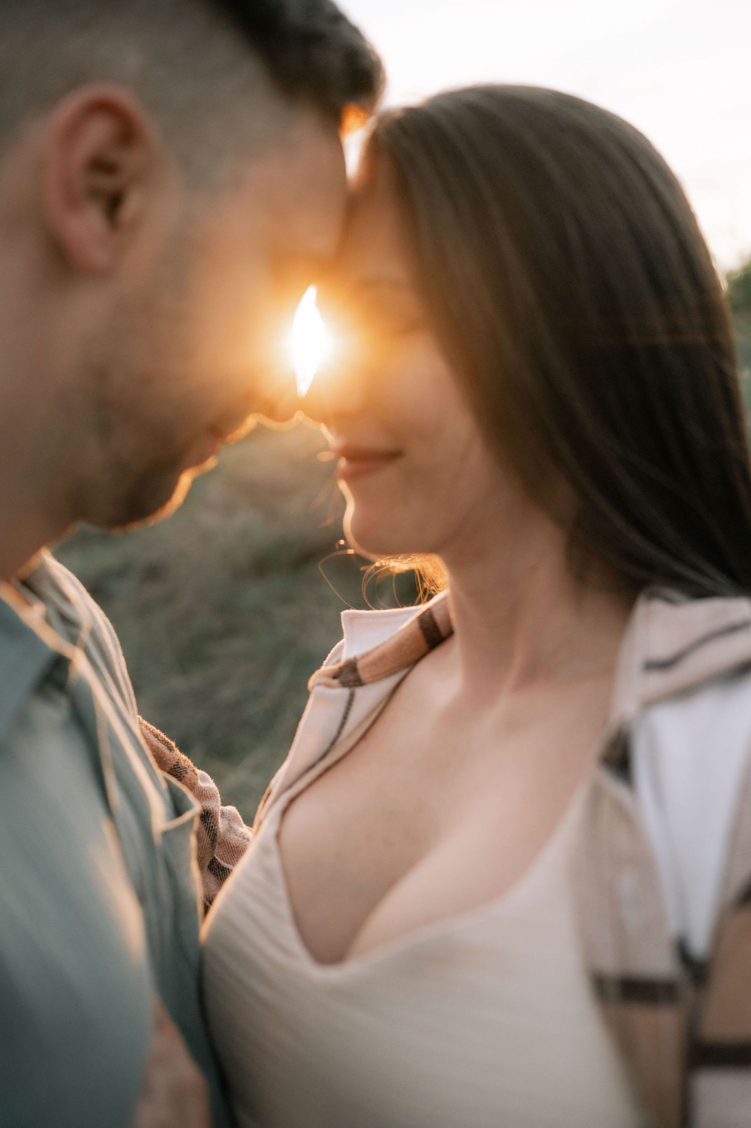 Romantic couple sharing an intimate moment at sunset with sun flare between their faces.