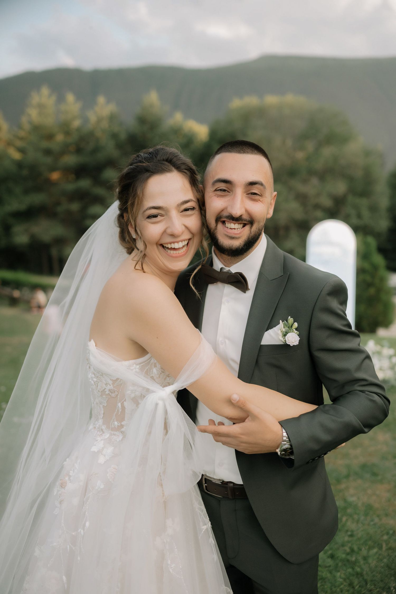 A joyful wedding moment captured outdoors with mountains and greenery creating a scenic backdrop.