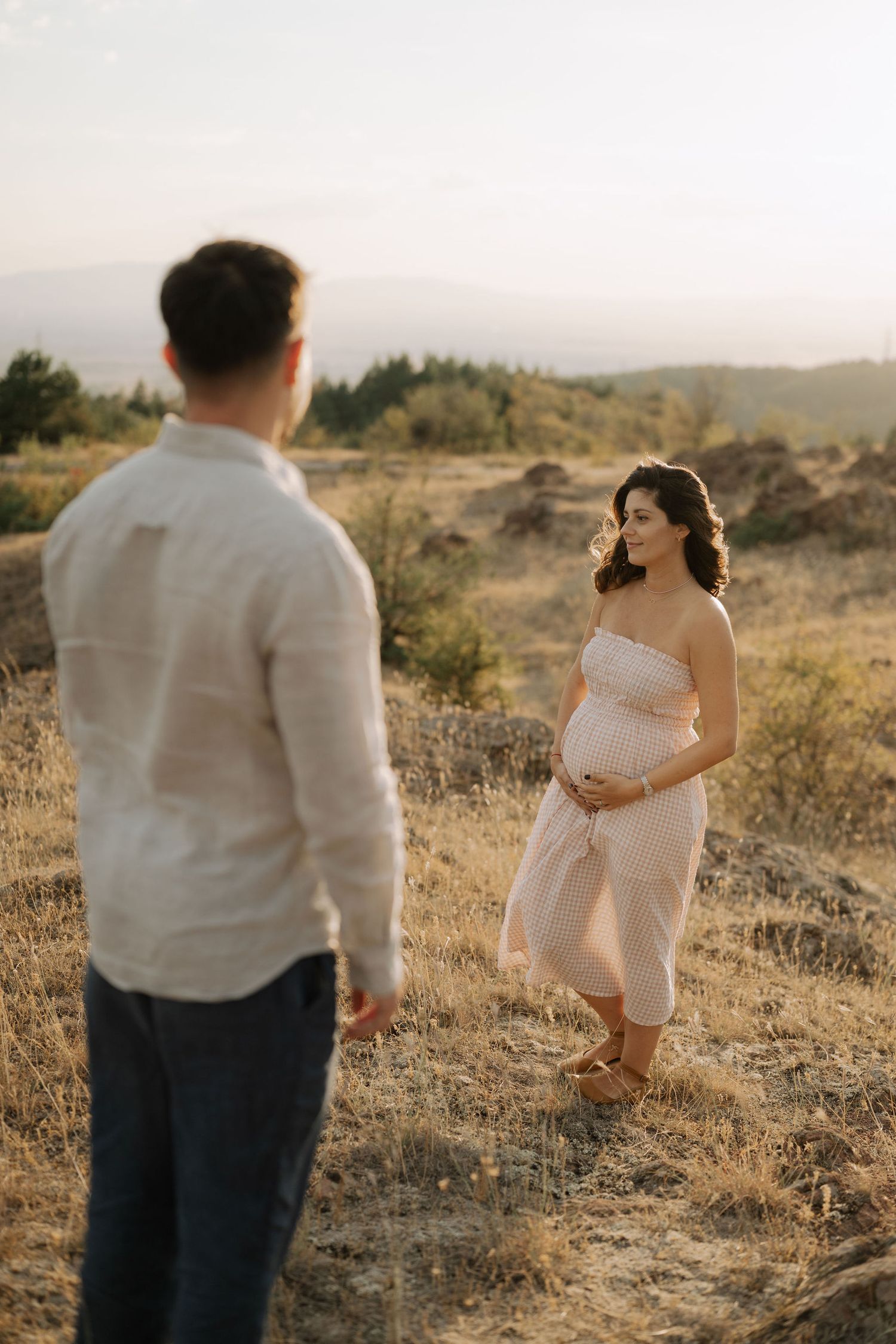 A couple poses for maternity photos in a golden field at sunset, capturing intimate moments in nature.