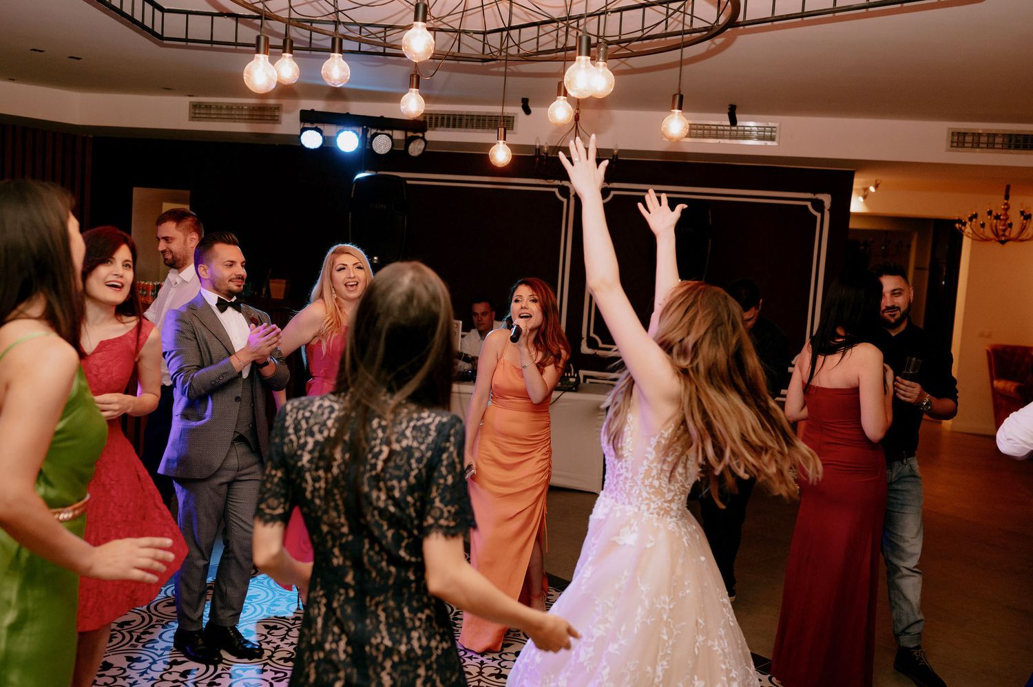 Wedding guests dance together on a dimly lit dance floor during a reception celebration.