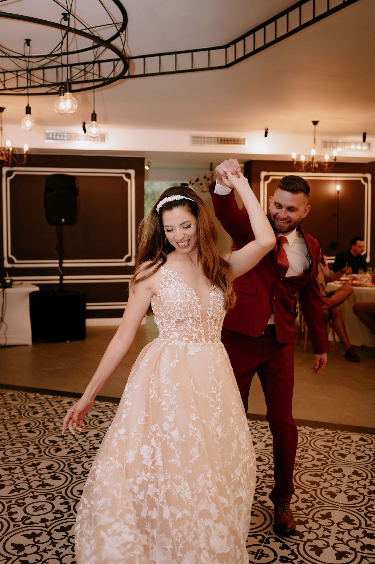 A couple dances together on a patterned floor at a wedding reception in warm lighting.