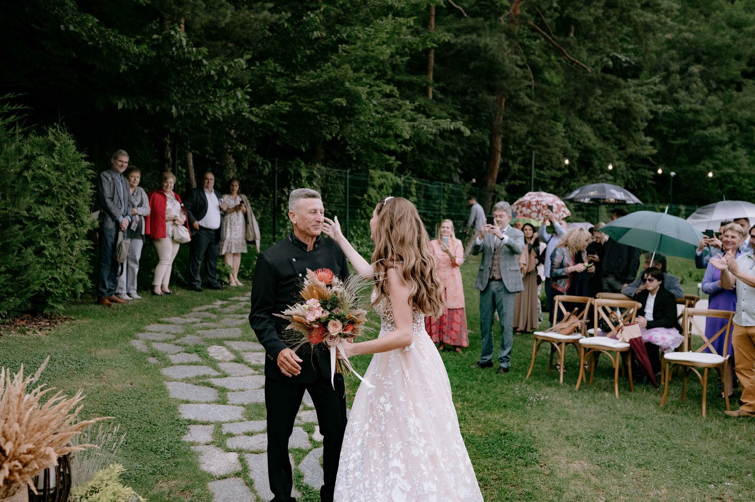A couple celebrates their first dance at an outdoor garden wedding reception with guests watching from wooden chairs.