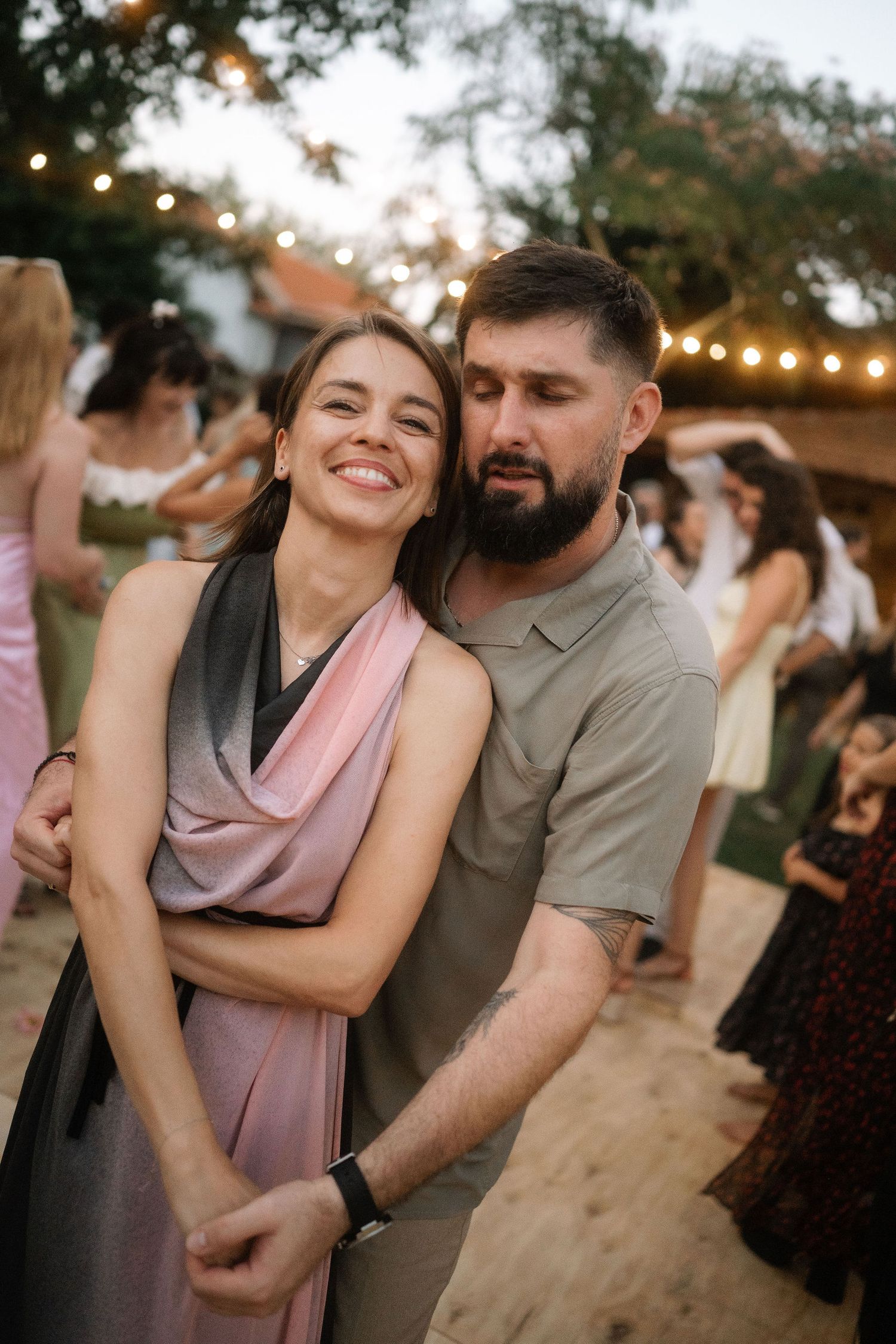 A couple shares joyful moments dancing together at an outdoor party with string lights in the background.