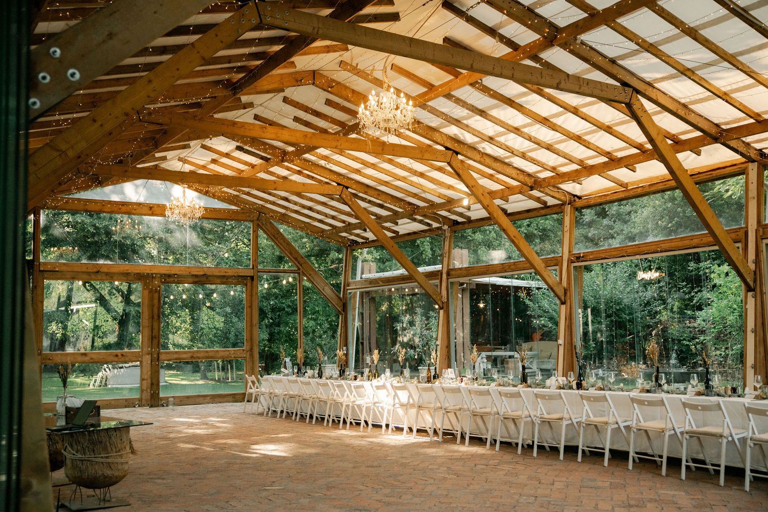 Long rustic wooden pavilion with exposed beams and string lights set up for an outdoor wedding reception.