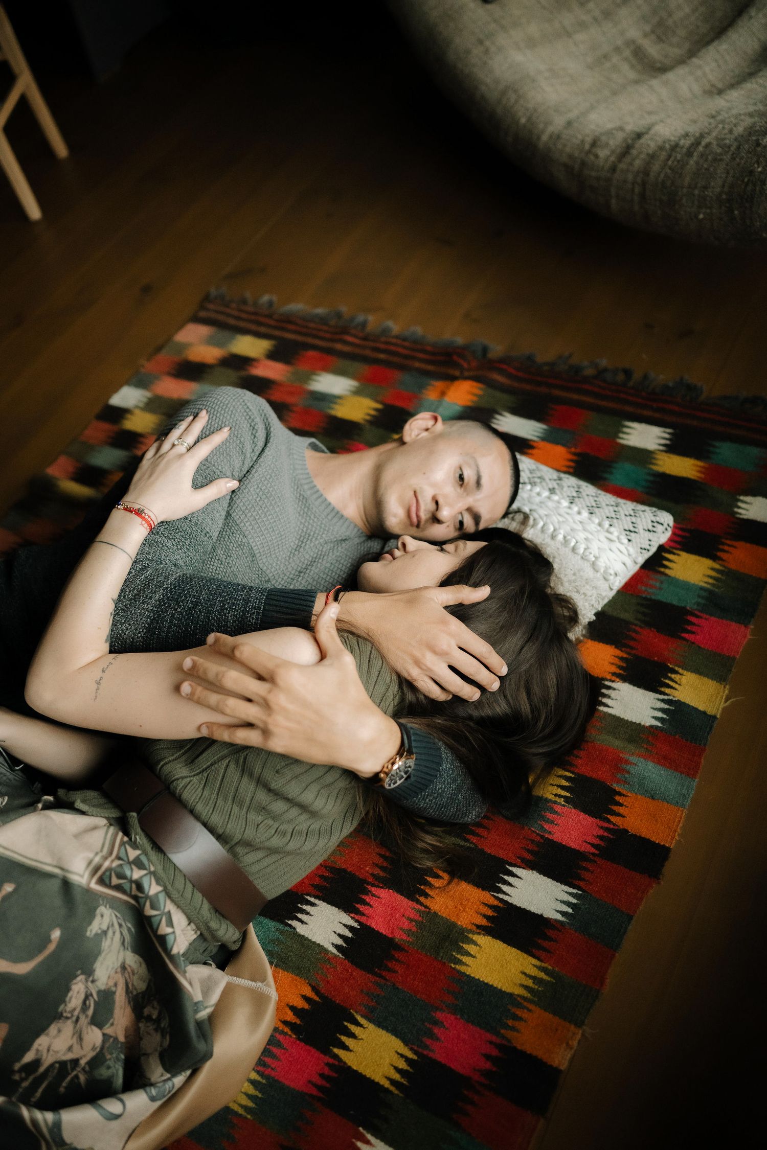 A person lies on a colorful geometric patterned rug in a dimly lit room.
