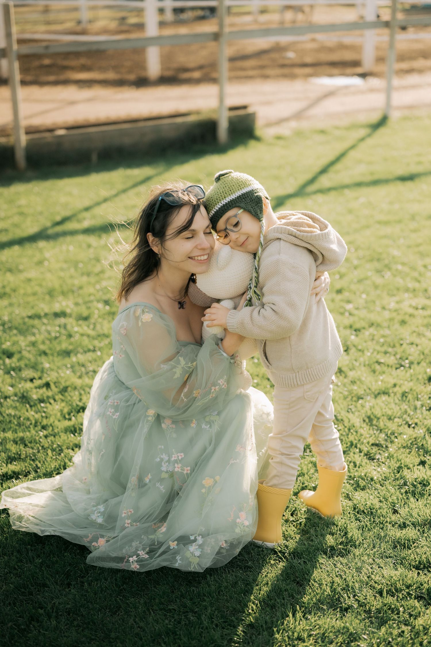 A tender moment captured in a sunlit garden as a parent and child share loving embraces on the grass.