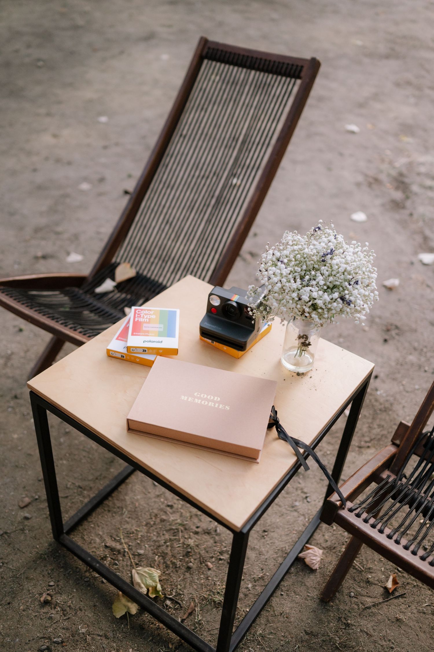 A minimalist wooden table with black metal legs holds playing cards and delicate baby's breath flowers on a concrete floor.