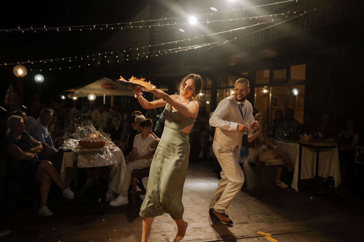 Couples dancing together at a nighttime outdoor celebration with string lights illuminating the scene.