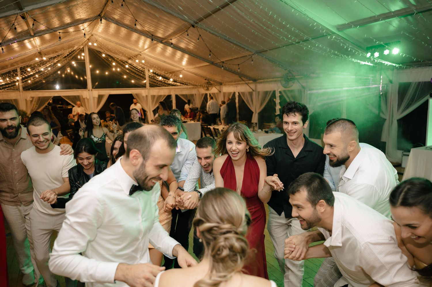 Wedding guests dance and celebrate on a green-lit dance floor during an energetic reception party.