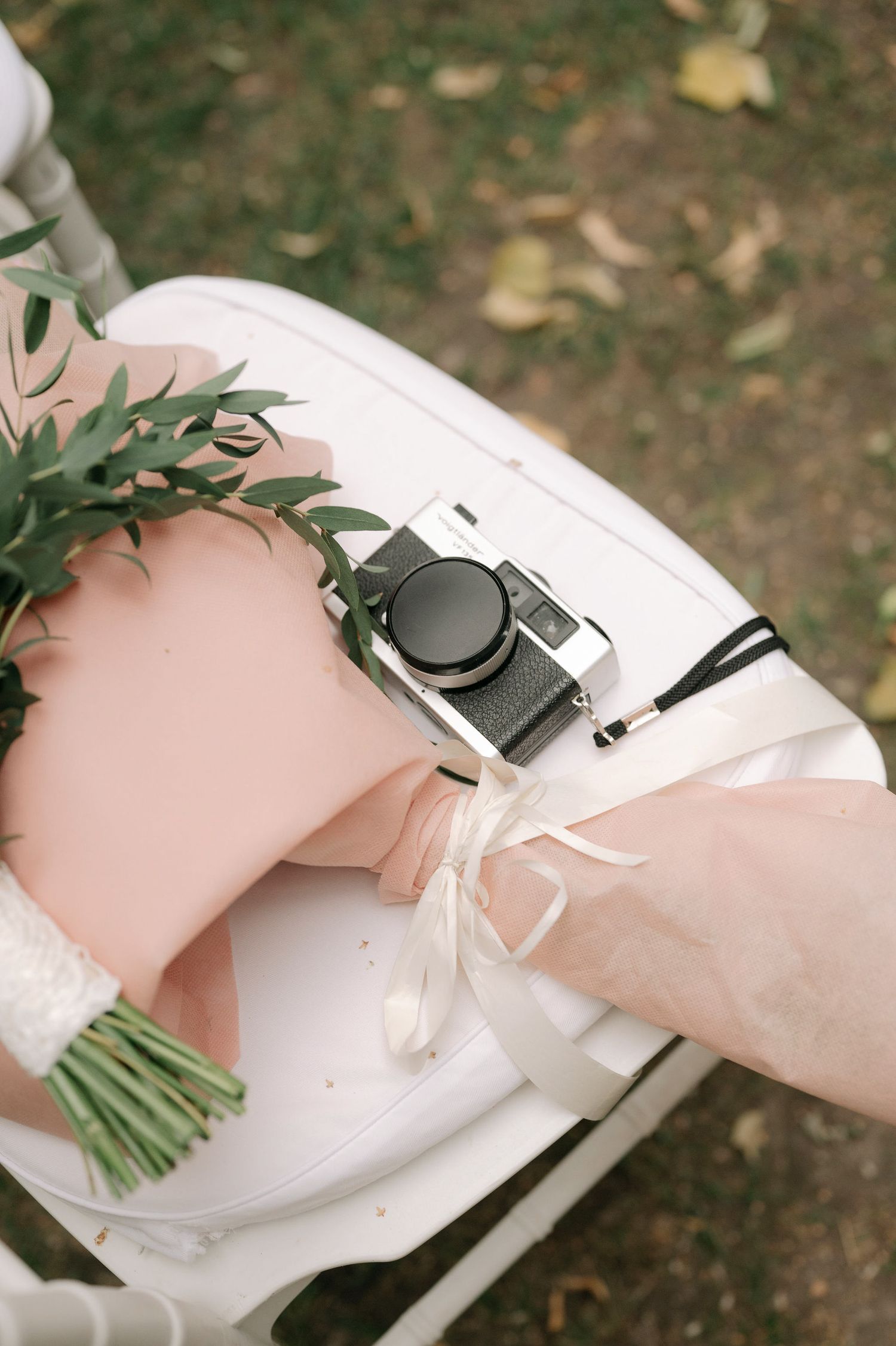 A white wedding shoe with floral accents rests on a grassy outdoor surface.
