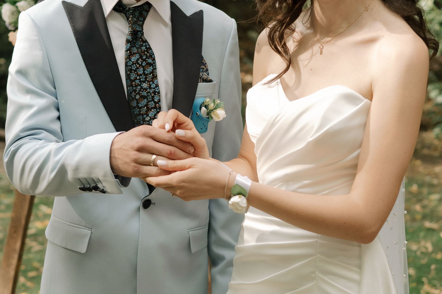 A couple in wedding attire exchange rings during an outdoor ceremony in a garden setting.