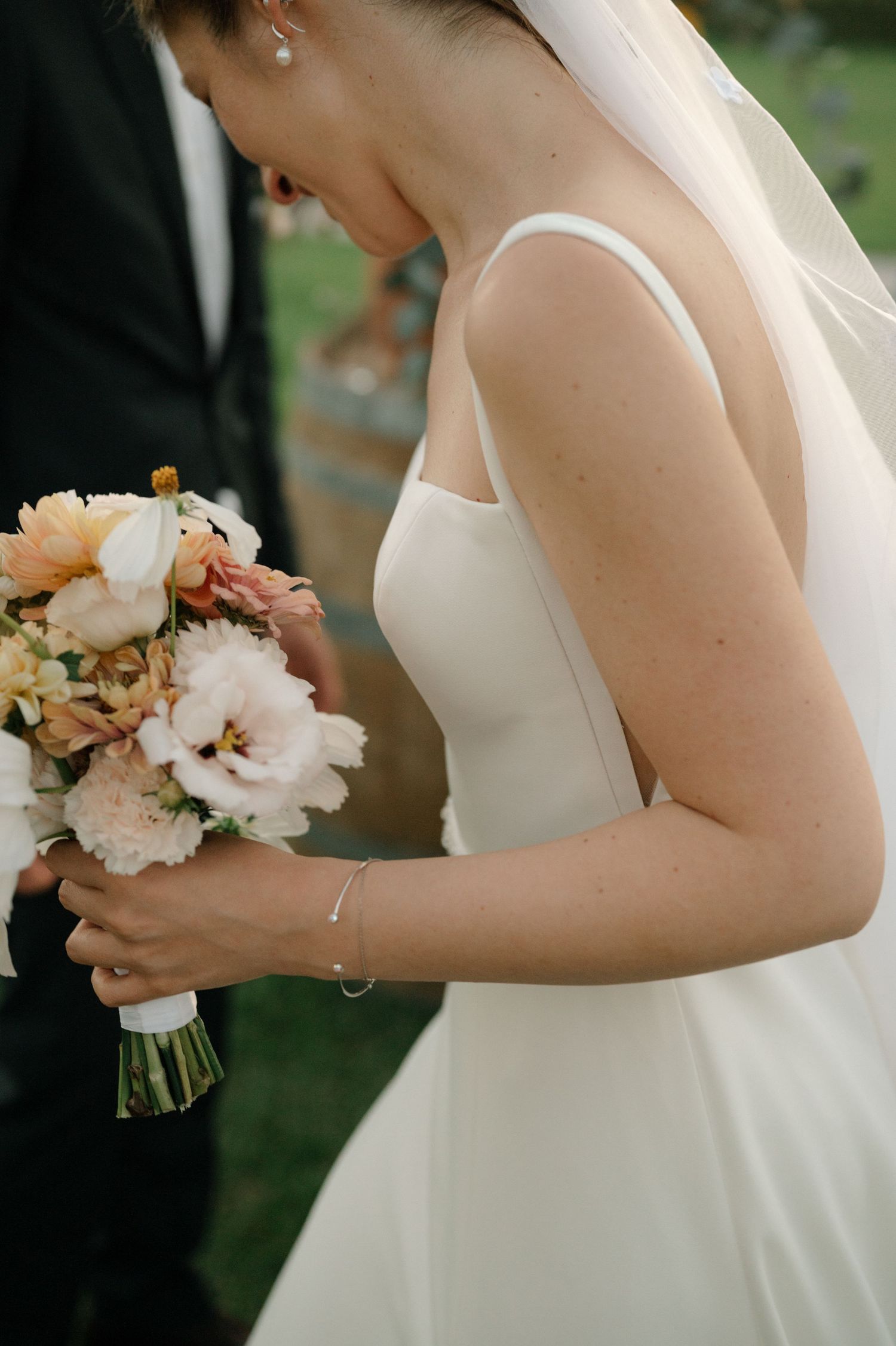 Close-up series of a bride in a white wedding dress holding a delicate pink and white floral bouquet during an outdoor ceremony.