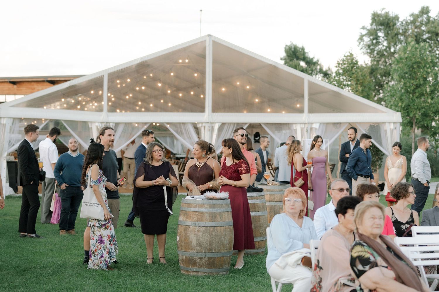 Wedding guests dance and celebrate under a white tent decorated with string lights during an outdoor reception party.