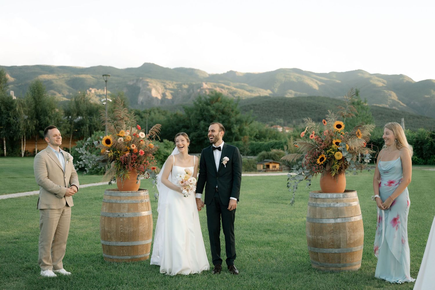 Outdoor wedding ceremony setup with wine barrels and floral arrangements against a scenic mountain backdrop.