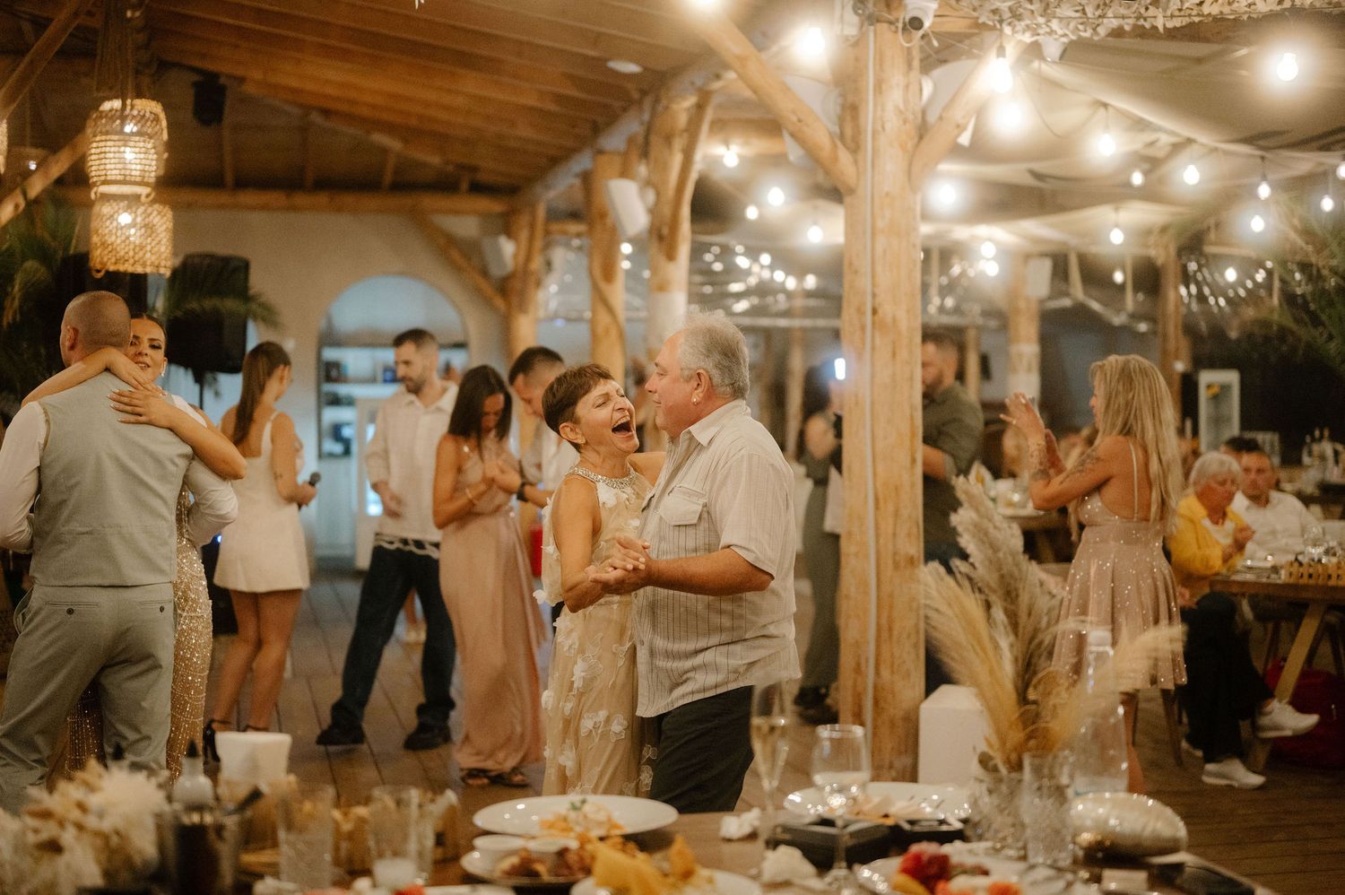 Guests mingle and socialize at a rustic indoor reception venue decorated with string lights and wooden beams.
