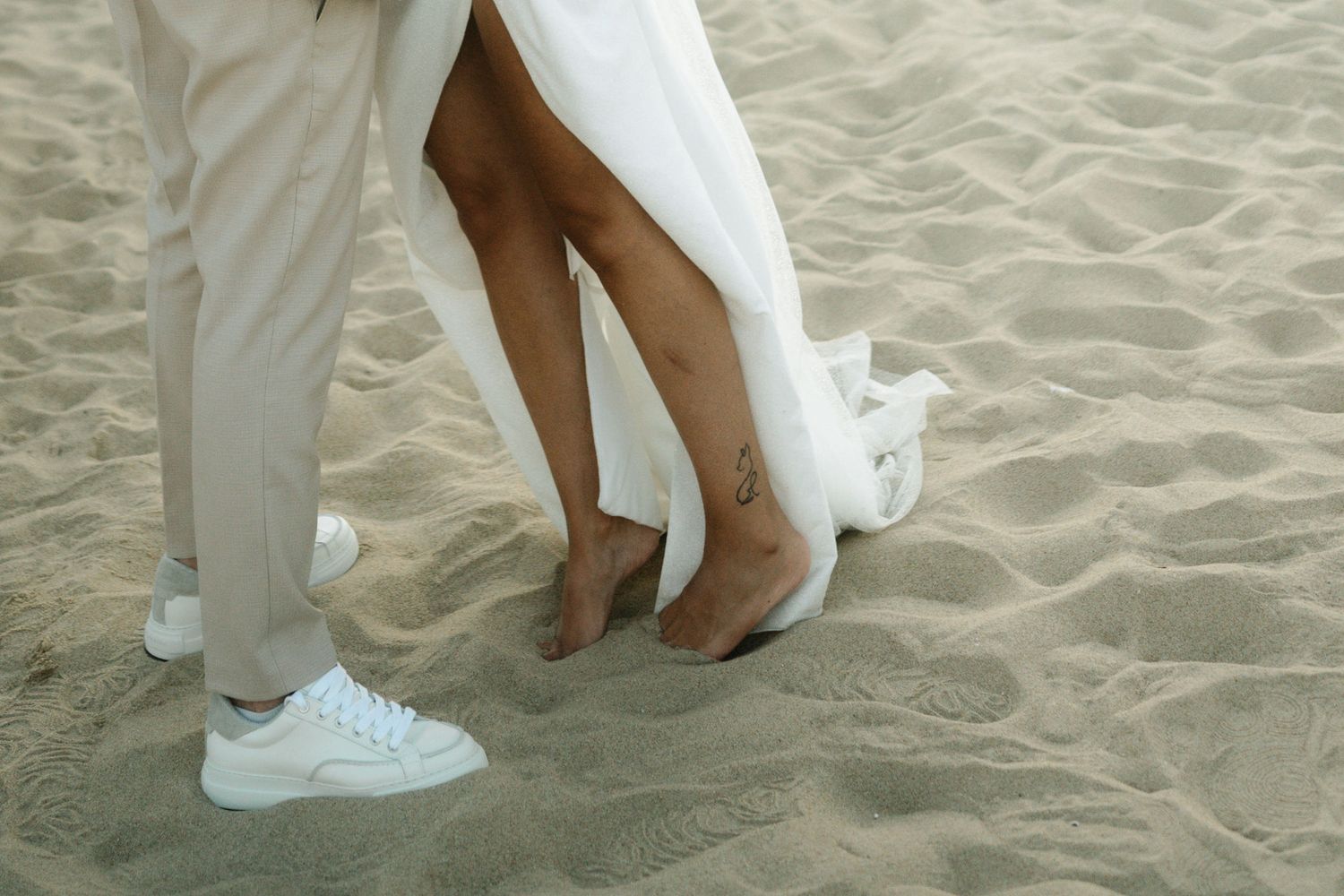 A couple's feet stand together on sandy beach during romantic wedding photoshoot.