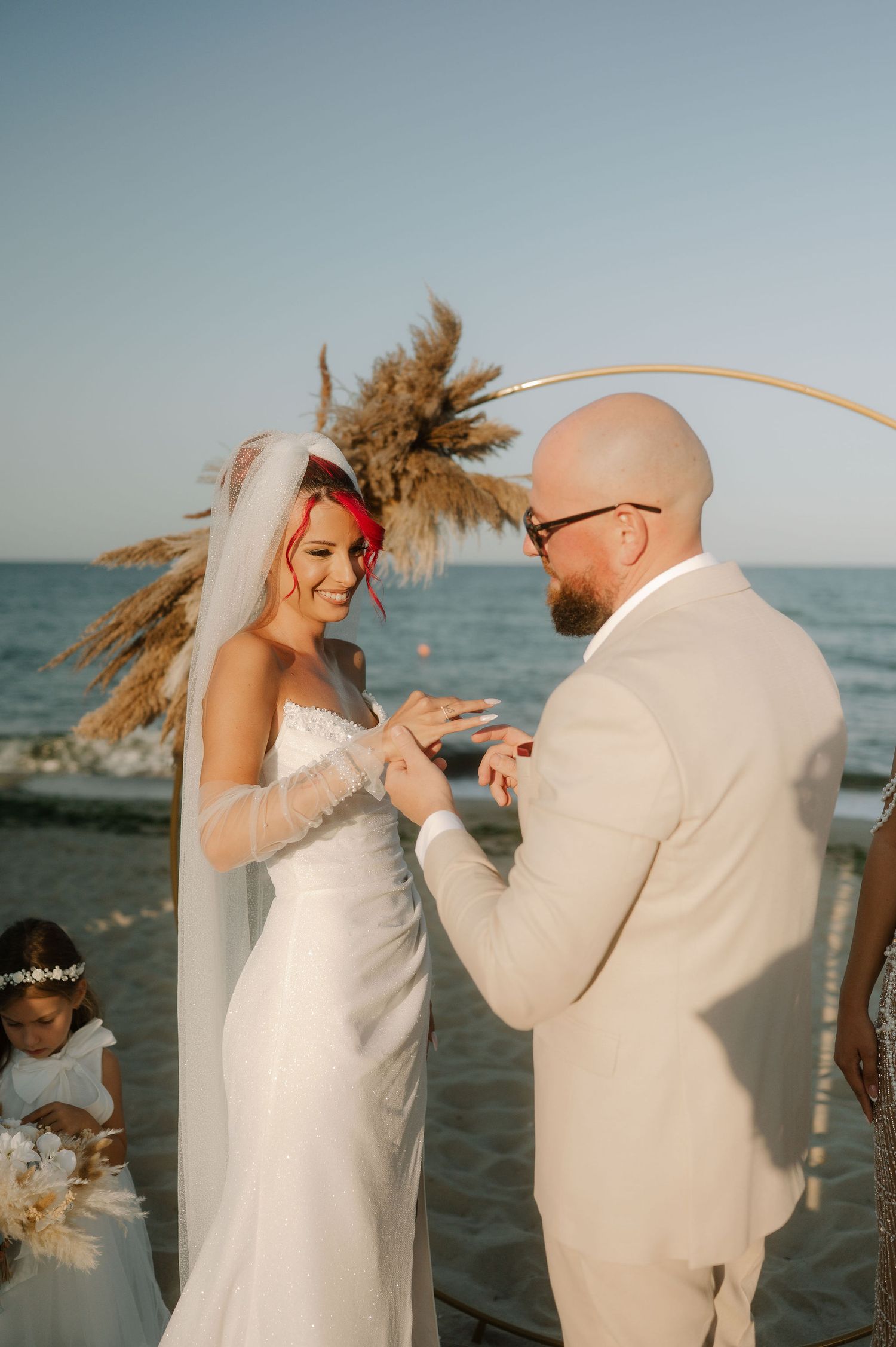 A couple in white outfits dances playfully together by the ocean at sunset, their movements captured in a series of photos.