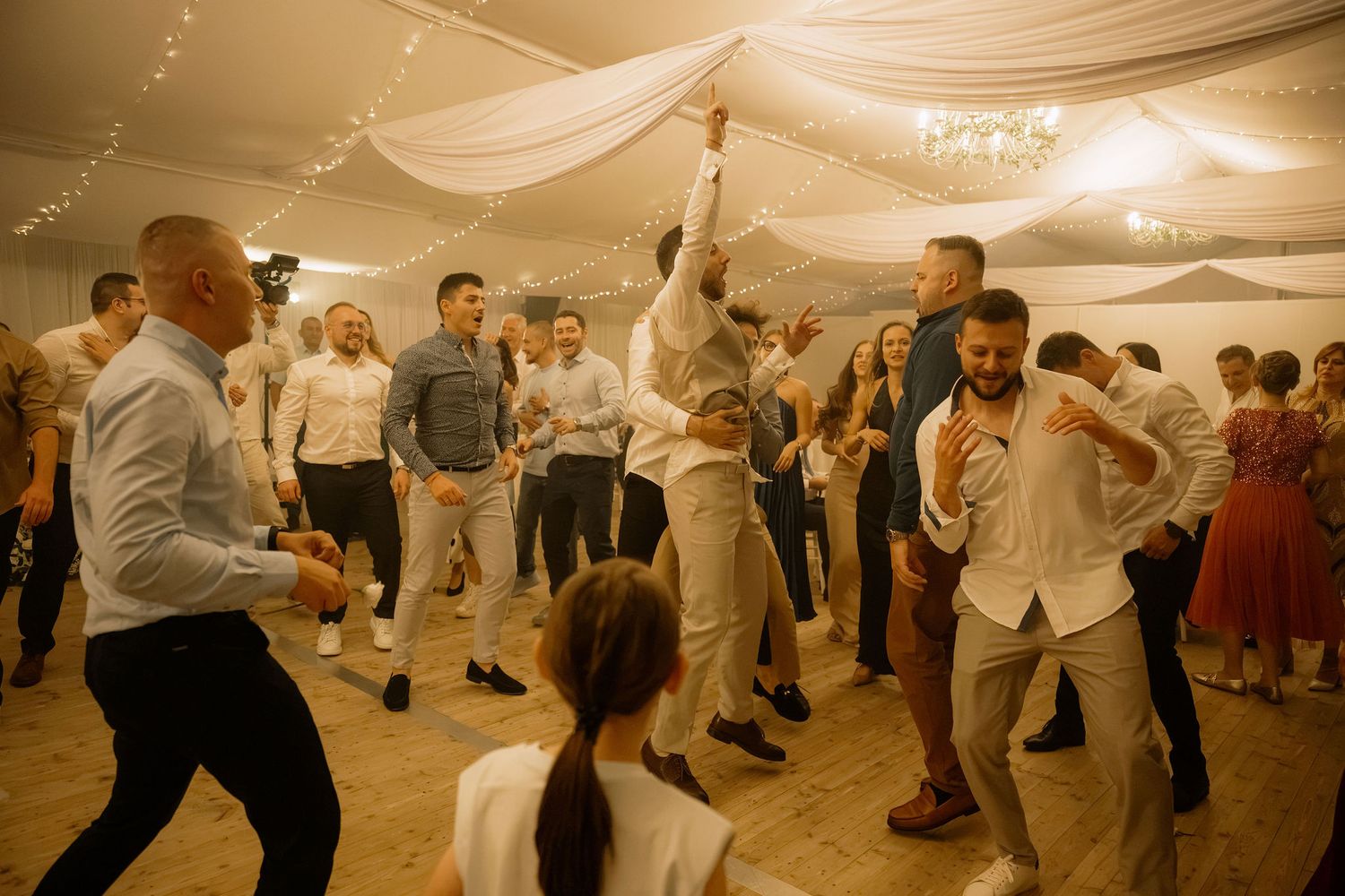 Guests dancing energetically at a wedding reception inside a decorated tent venue.